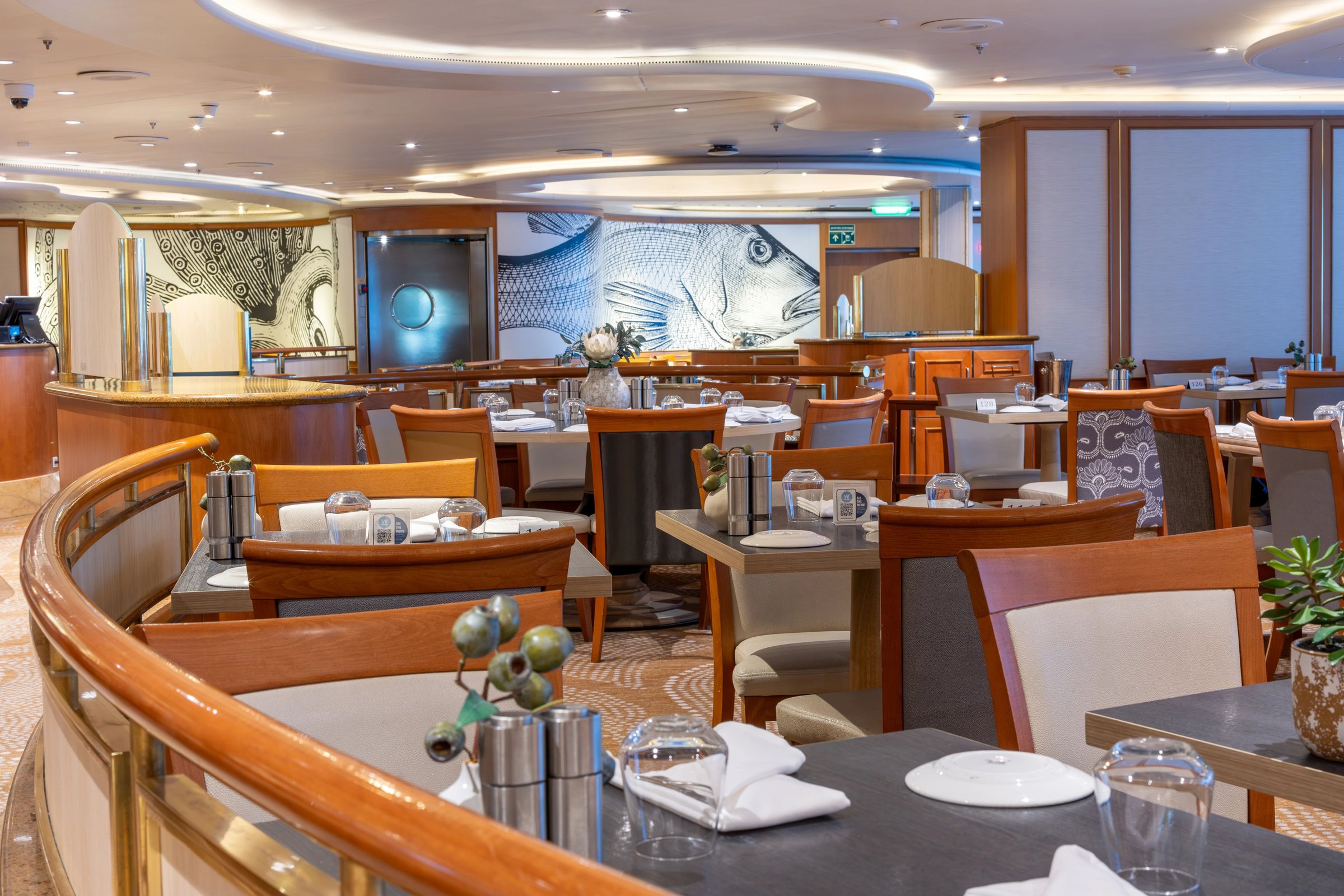 Carnival Adventure Waterfront restaurant dining room with curved rail and warm wood furnishings