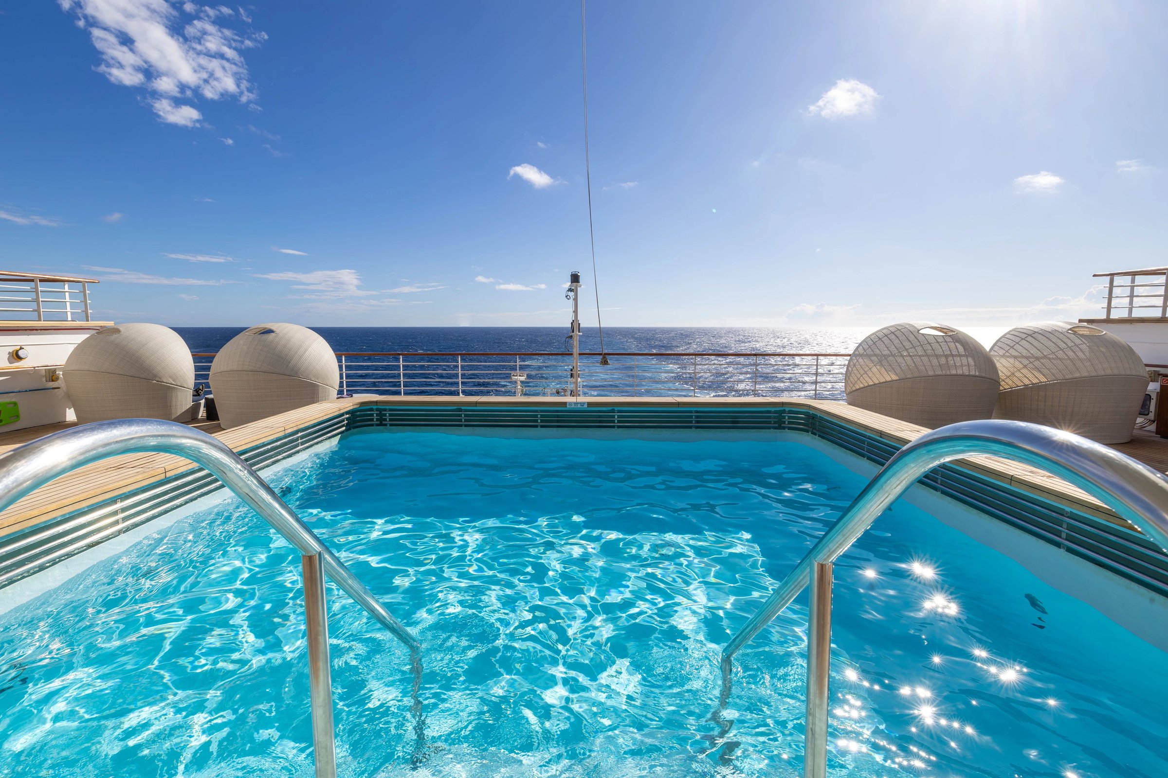 Carnival Adventure Oasis Pool close view with steps and cabana daybeds under bright blue sky