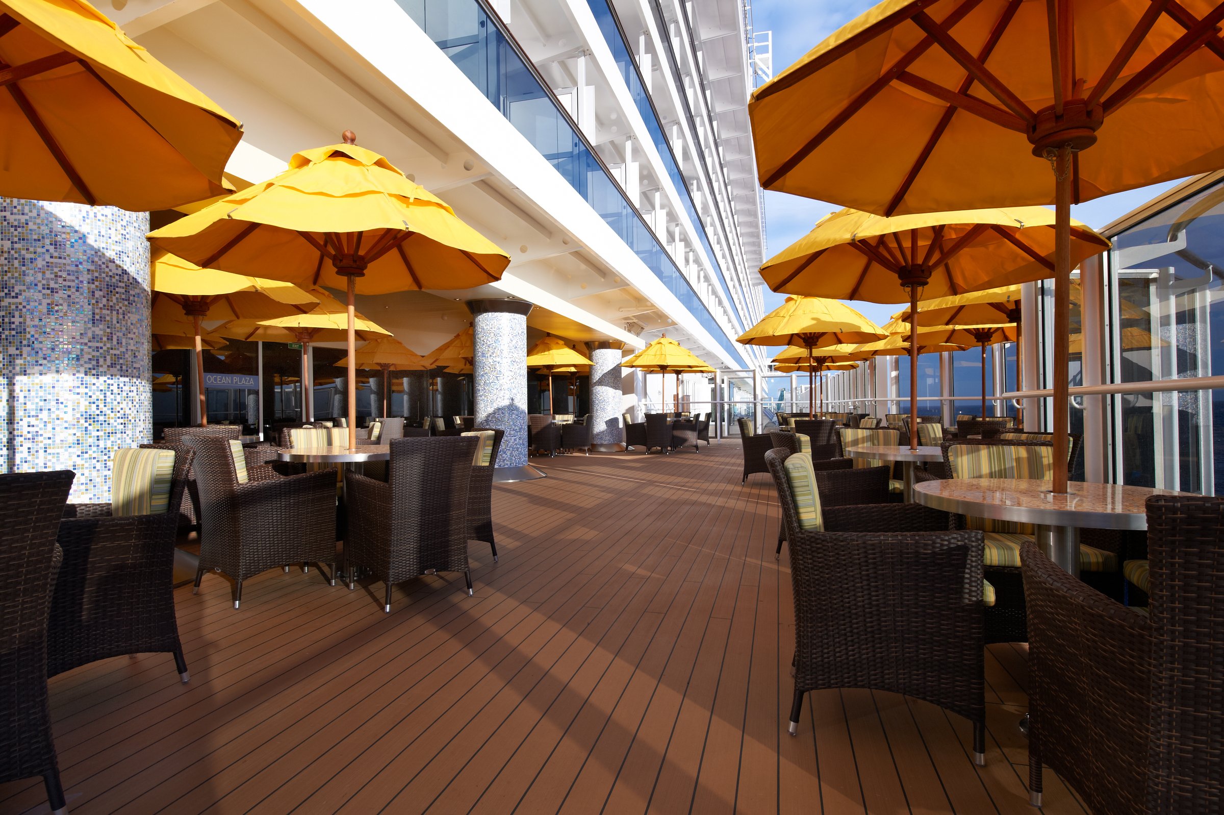 Carnival Breeze Plaza Bar lanai with wicker chairs and yellow umbrellas along the promenade