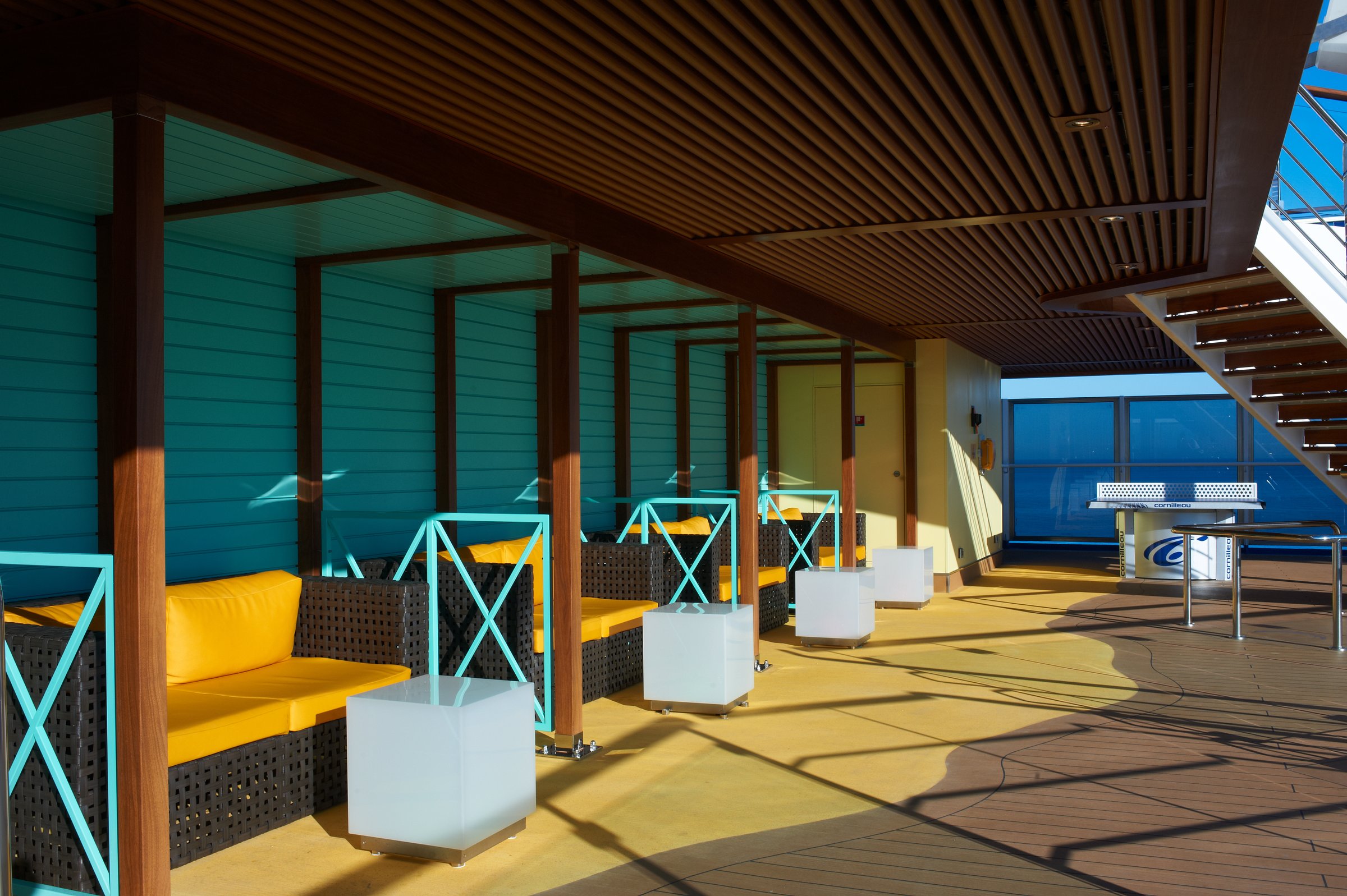 Carnival Breeze covered aft deck with teal walls, yellow cushioned seating and sunlit deck