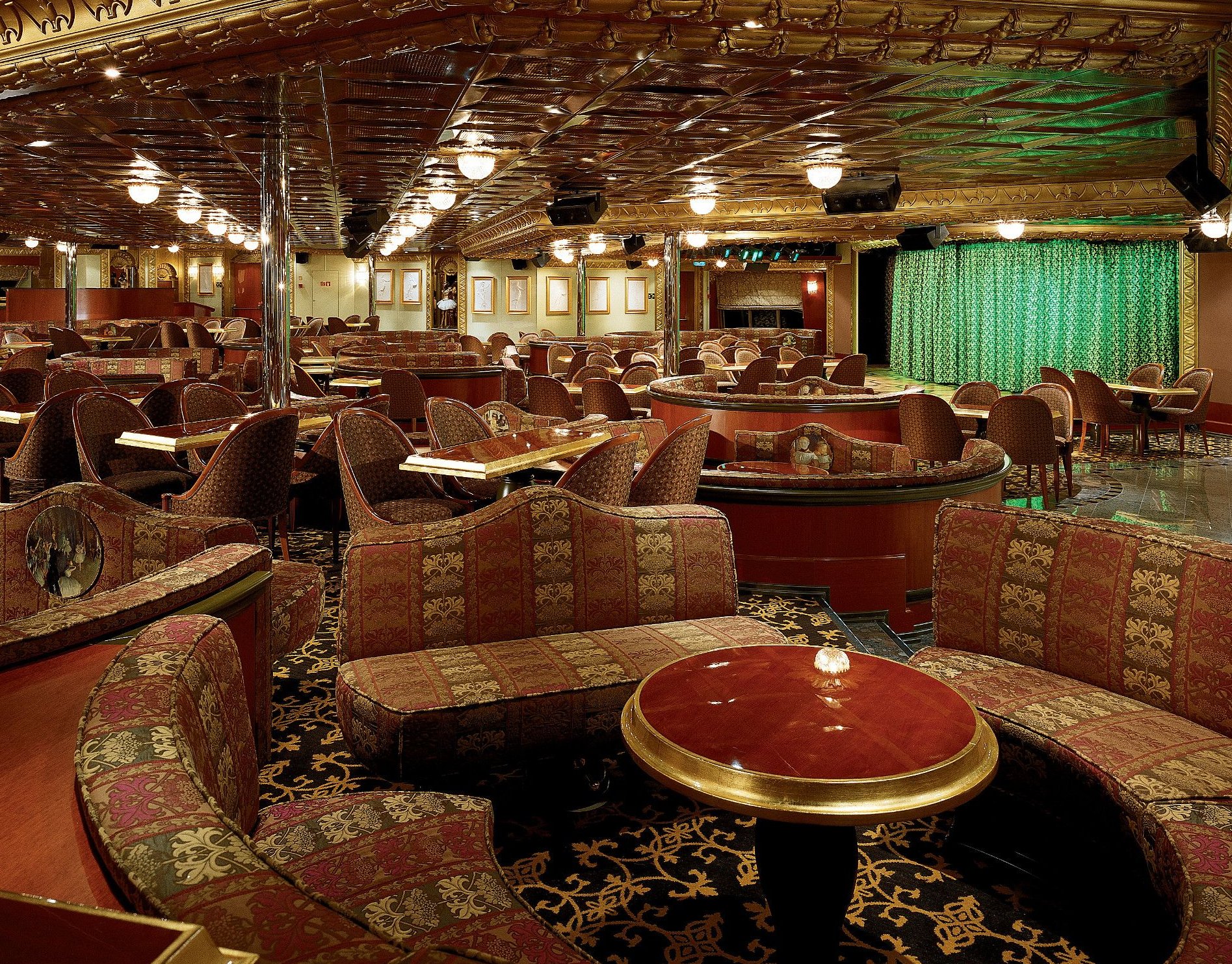 Carnival Conquest lounge with curved banquettes, red table and stage curtain