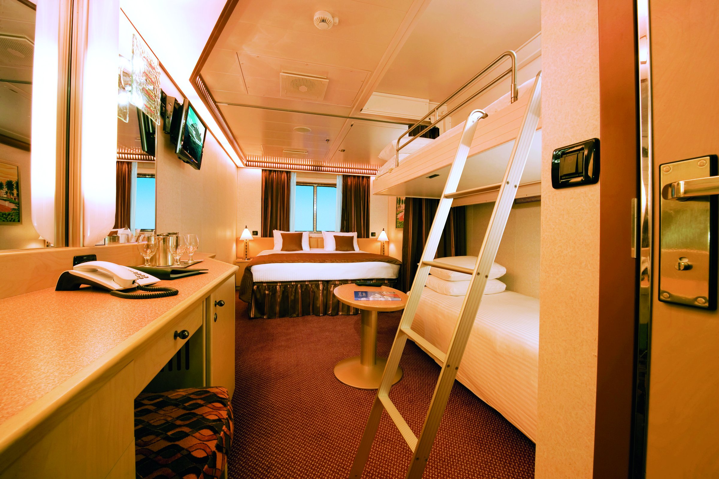 Carnival Dream interior stateroom with a double bed, upper bunk and built-in desk