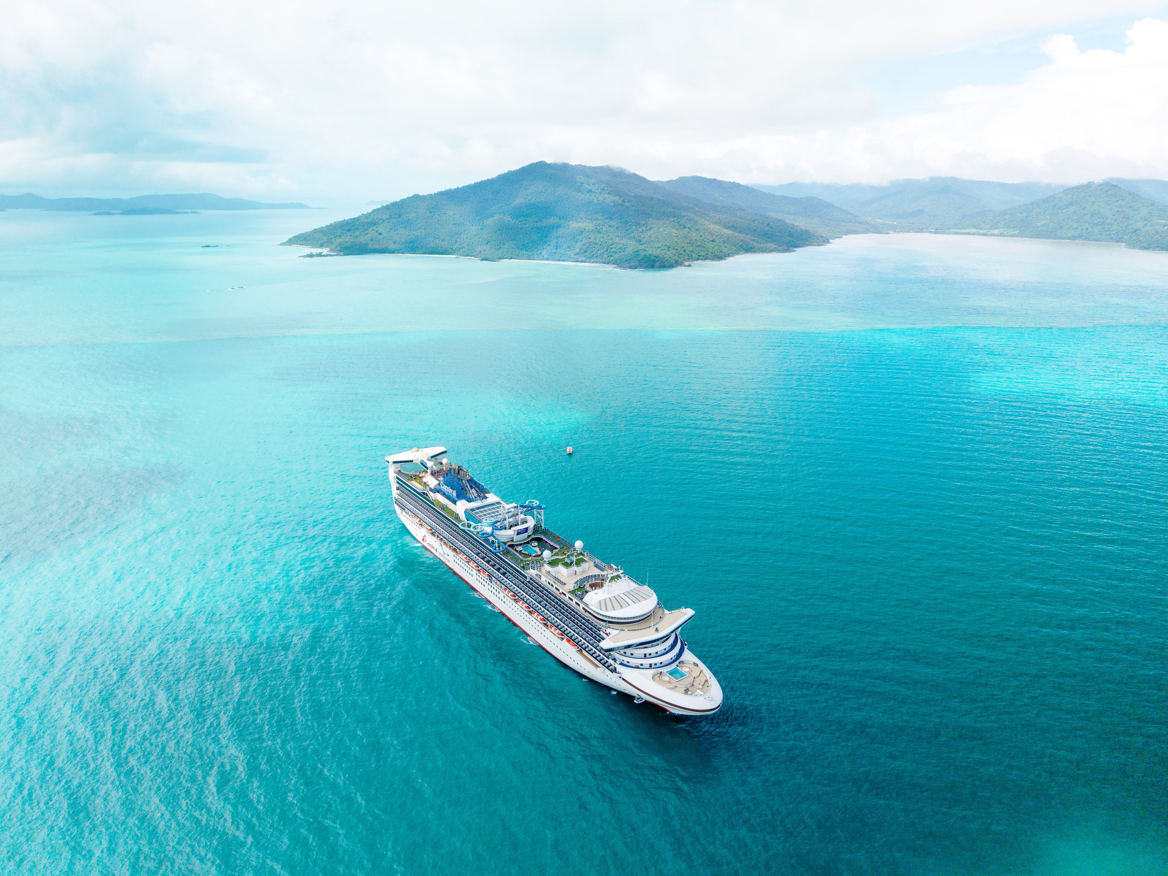 Carnival Encounter aerial at anchor in the Whitsundays with a green island and shallow turquoise water