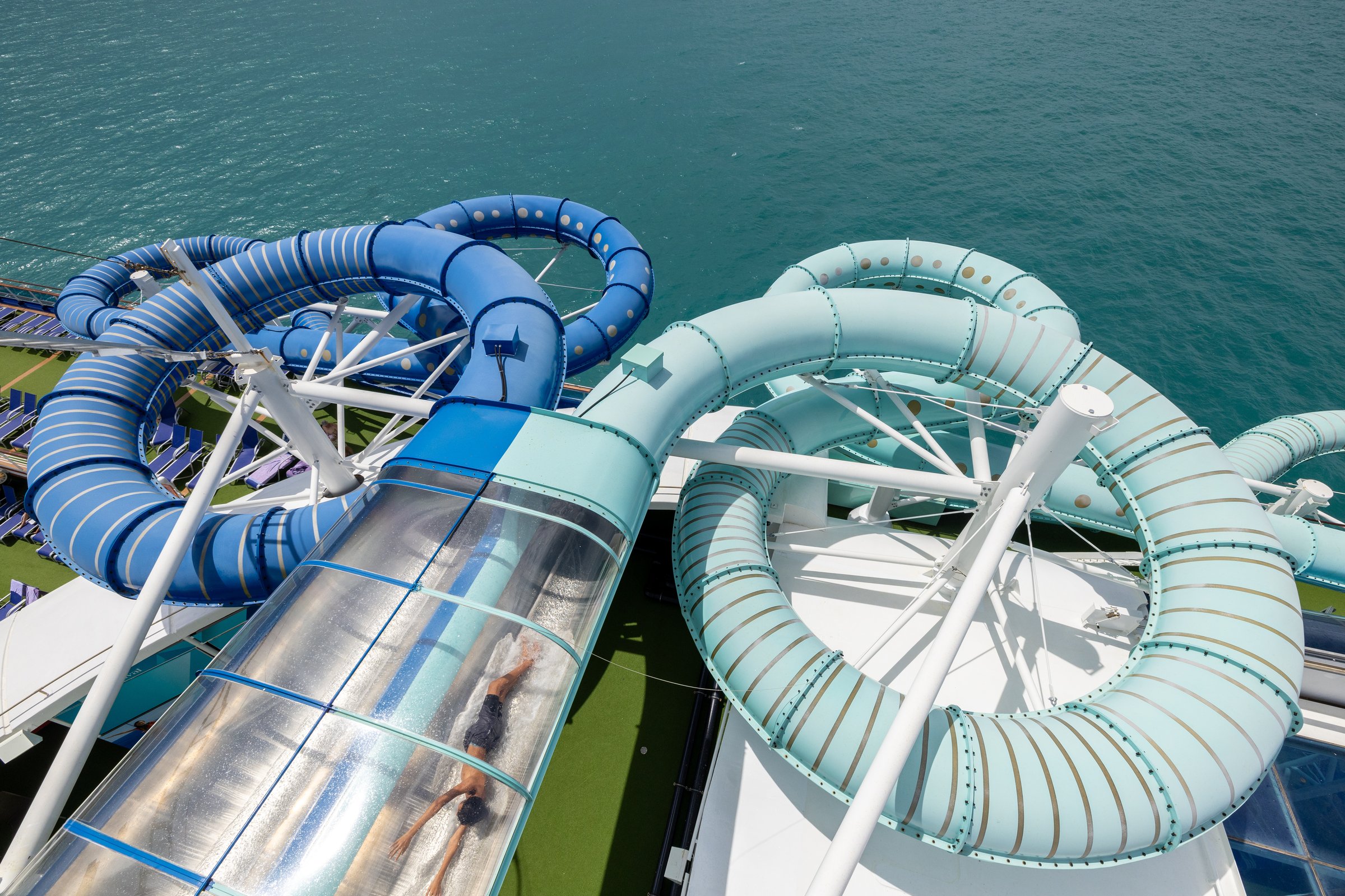 Carnival Encounter waterslides from above, blue and aqua spiral tubes over the sea