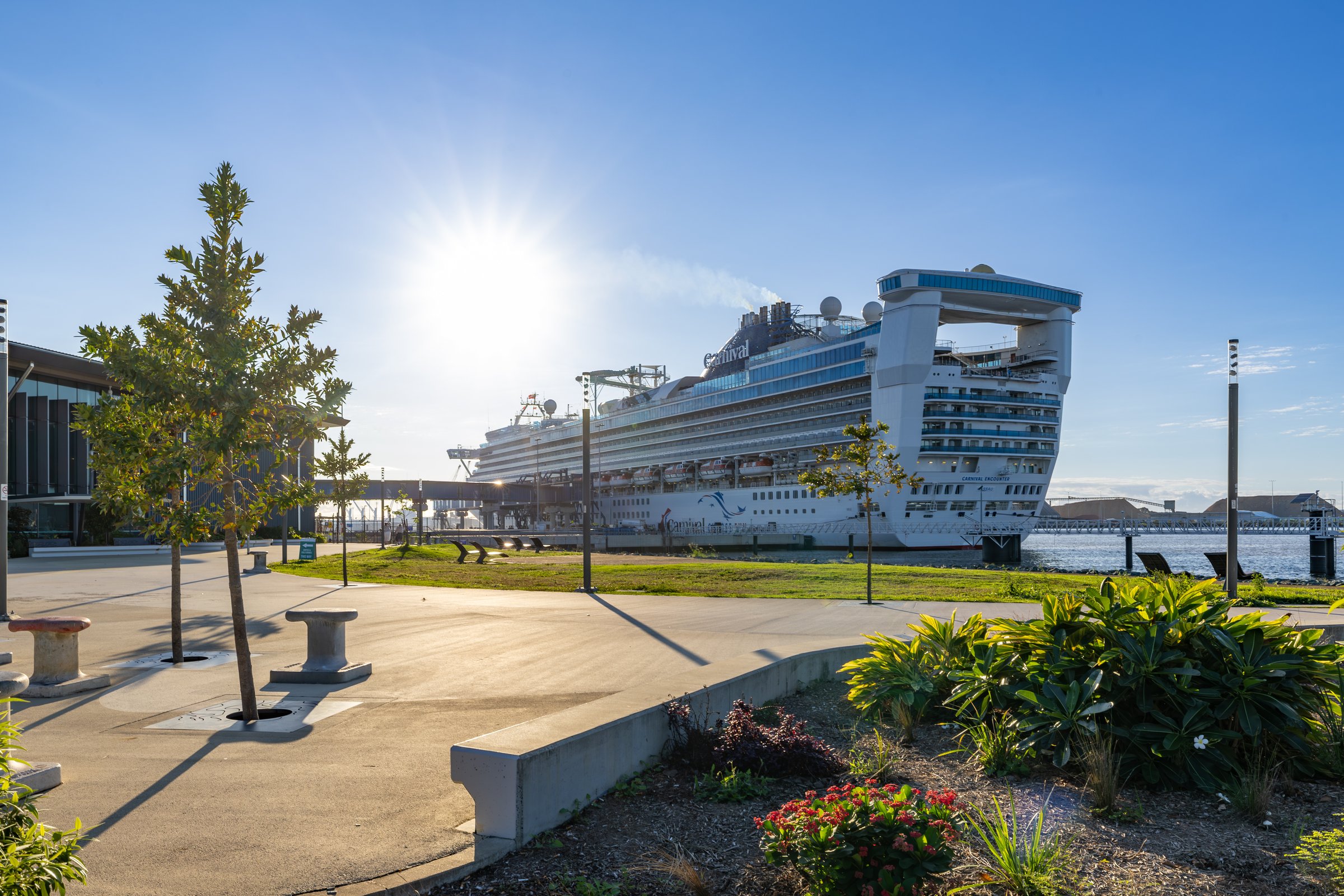 Carnival Encounter berthed at the Brisbane cruise terminal, seen across landscaped gardens on a sunny day