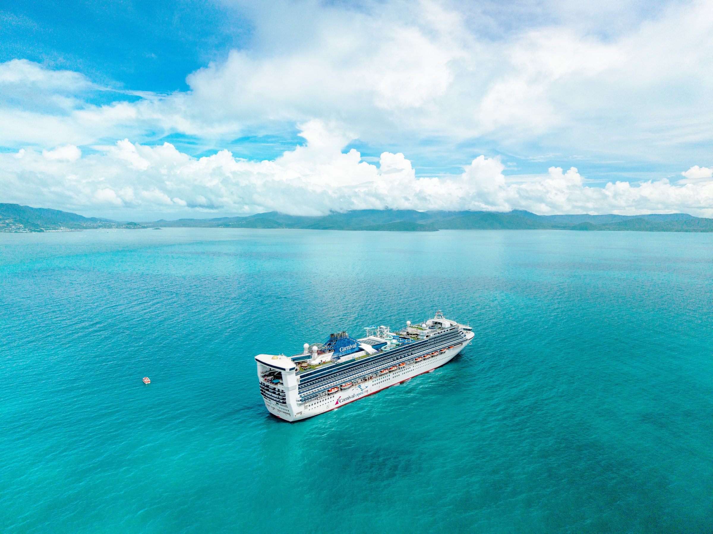 Carnival Encounter at anchor in turquoise water off Airlie Beach with green hills and white clouds behind