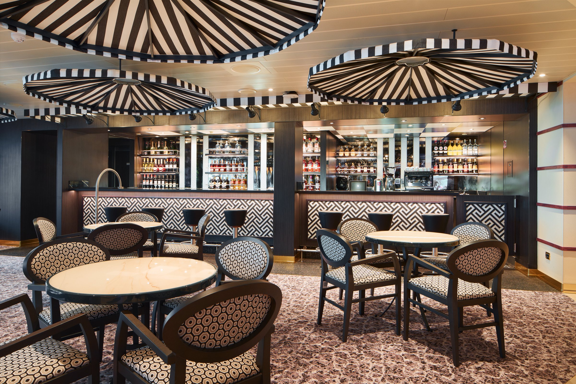 Carnival Firenze Tuscany lounge with striped parasol ceiling, geometric-pattern chairs and a back bar