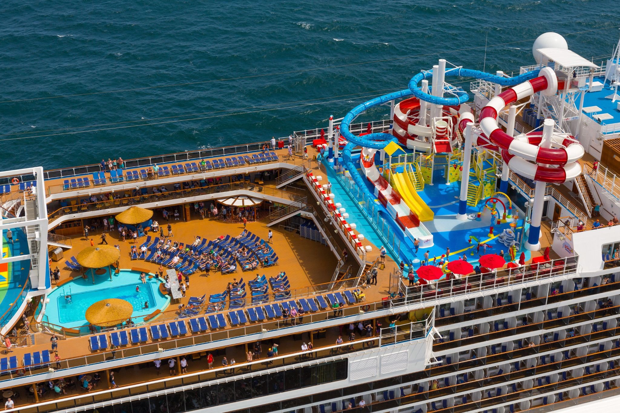 Aerial of Carnival Horizon WaterWorks slides above the aft pool deck with yellow umbrellas and loungers