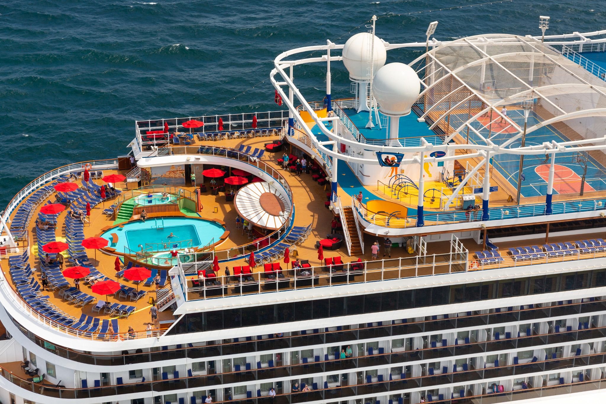 Aerial close-up of Carnival Horizon upper decks with a pool ringed by red umbrellas and loungers