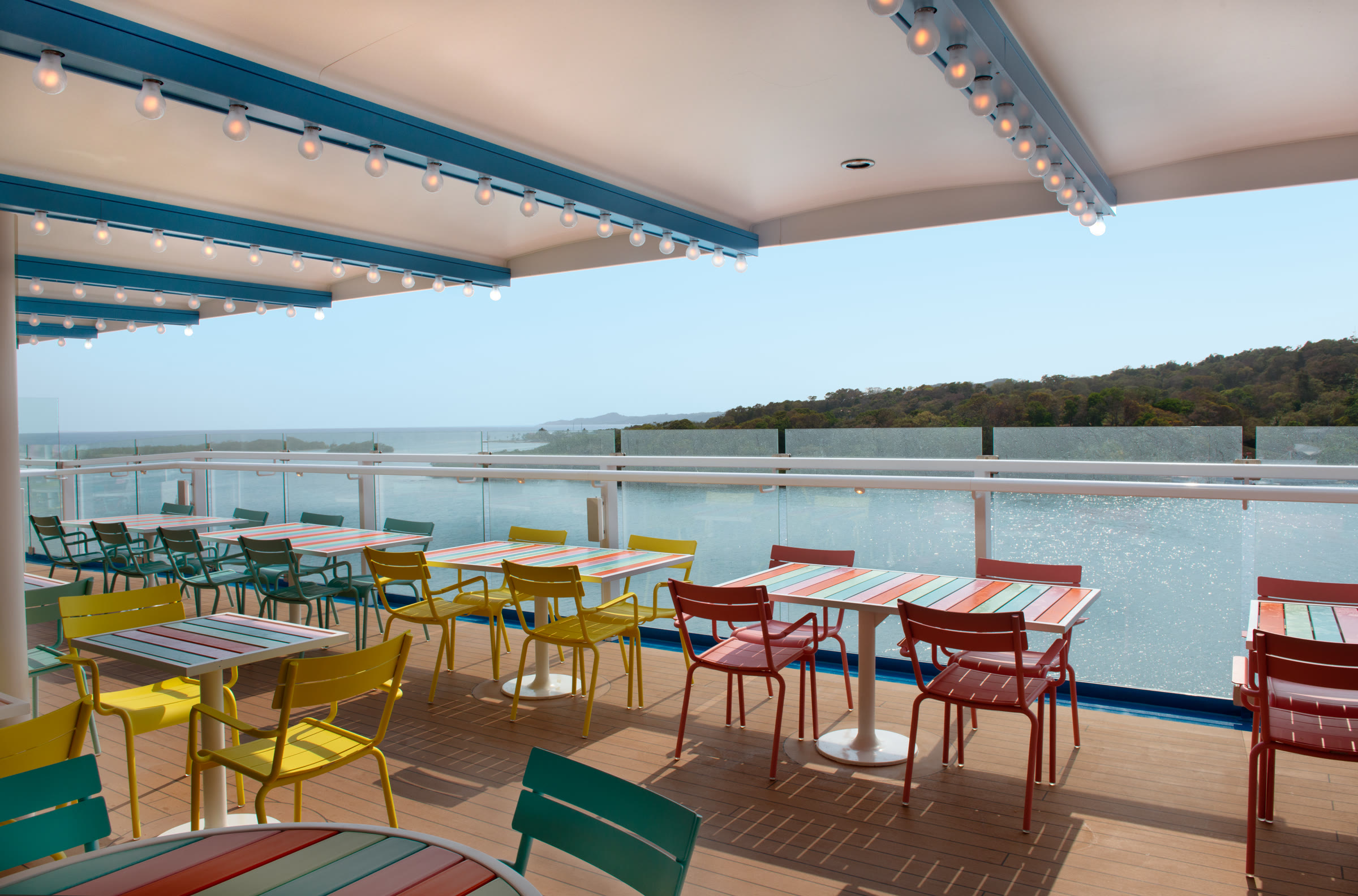 Sunny outdoor Shores dining deck overlooking turquoise water aboard Carnival Jubilee