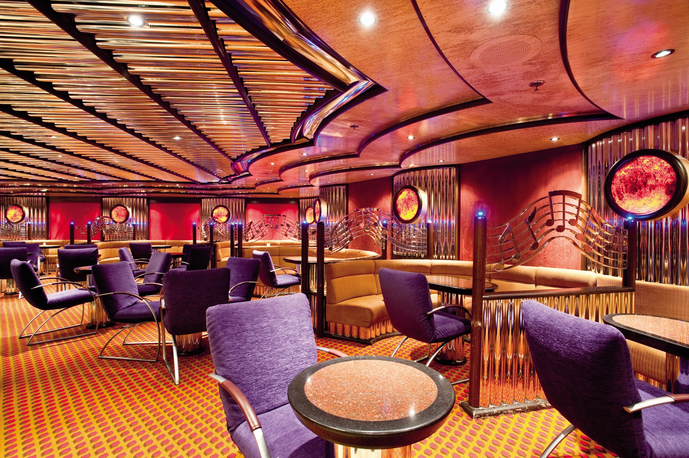 Carnival Legend Billie's piano bar with purple armchairs, patterned carpet and a curved wood ceiling