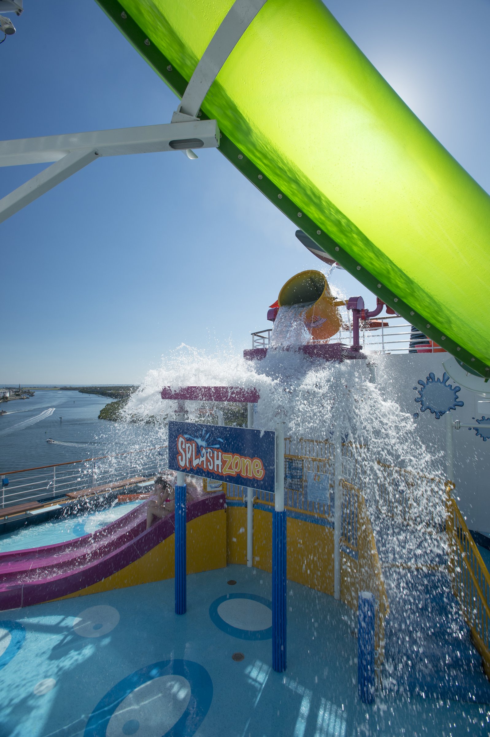 Carnival Legend WaterWorks water play area with a giant splashing bucket and green slide under a sunny blue sky