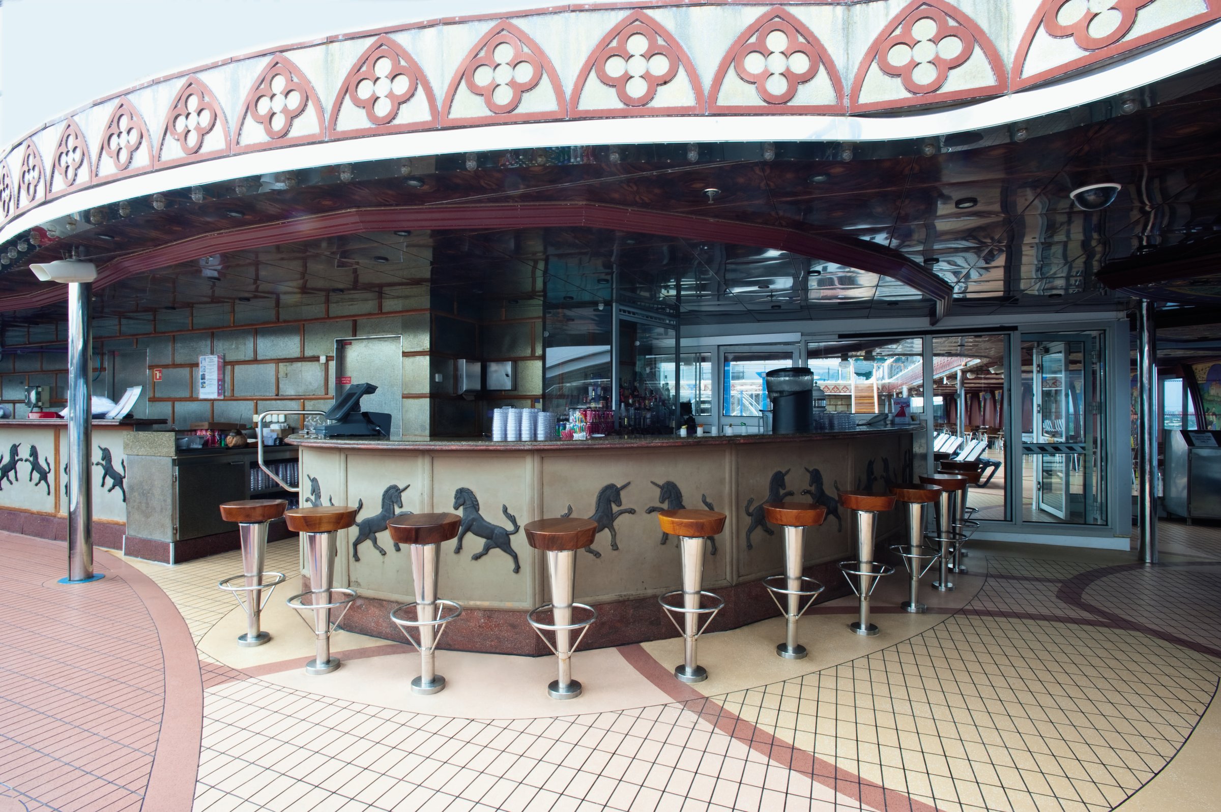 Carnival Legend Avalon pool bar with horse-motif counter, stools and tiled deck in bright daylight