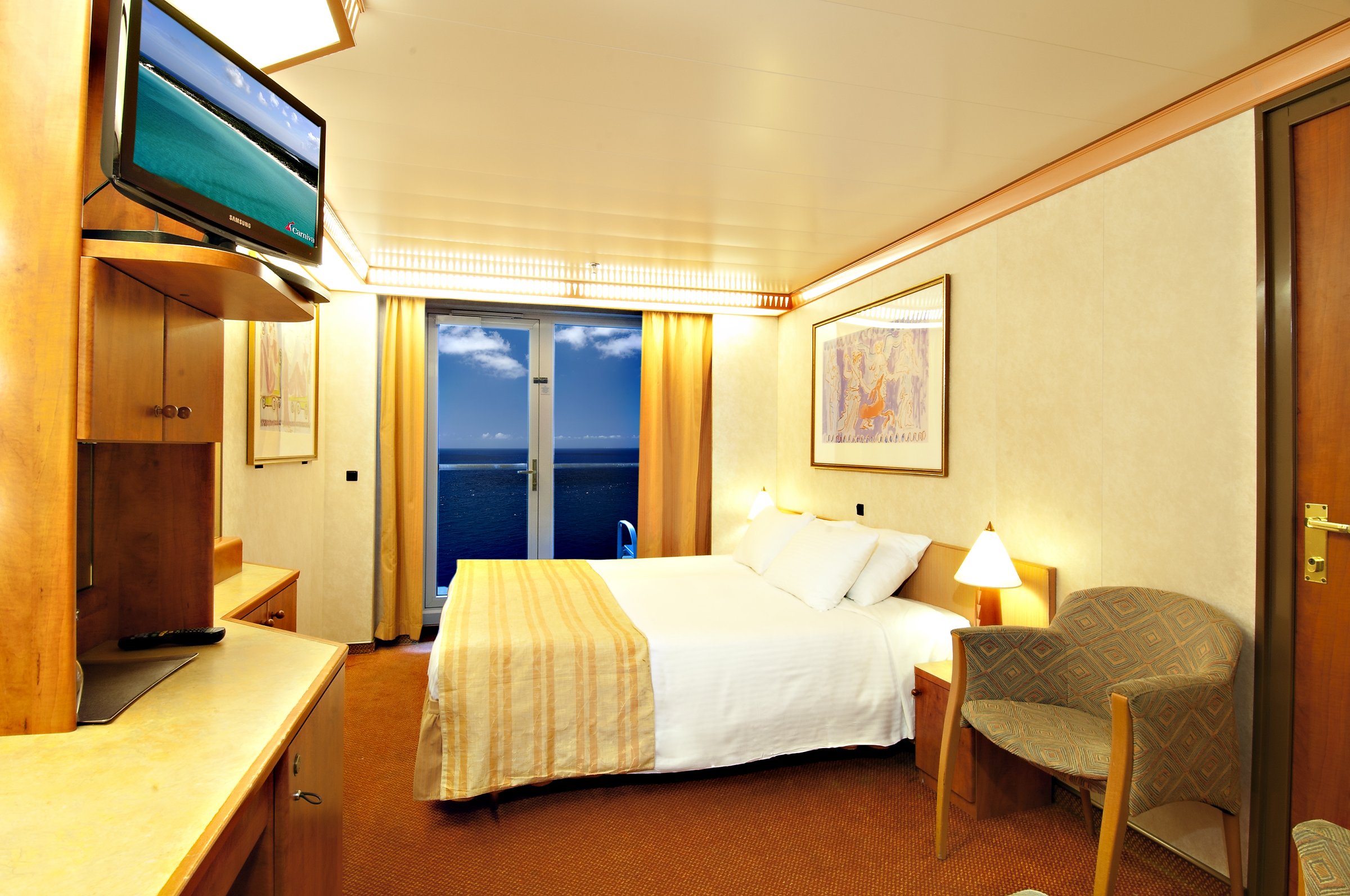 Carnival Legend balcony stateroom with a double bed, sitting area and sliding glass doors to the sea