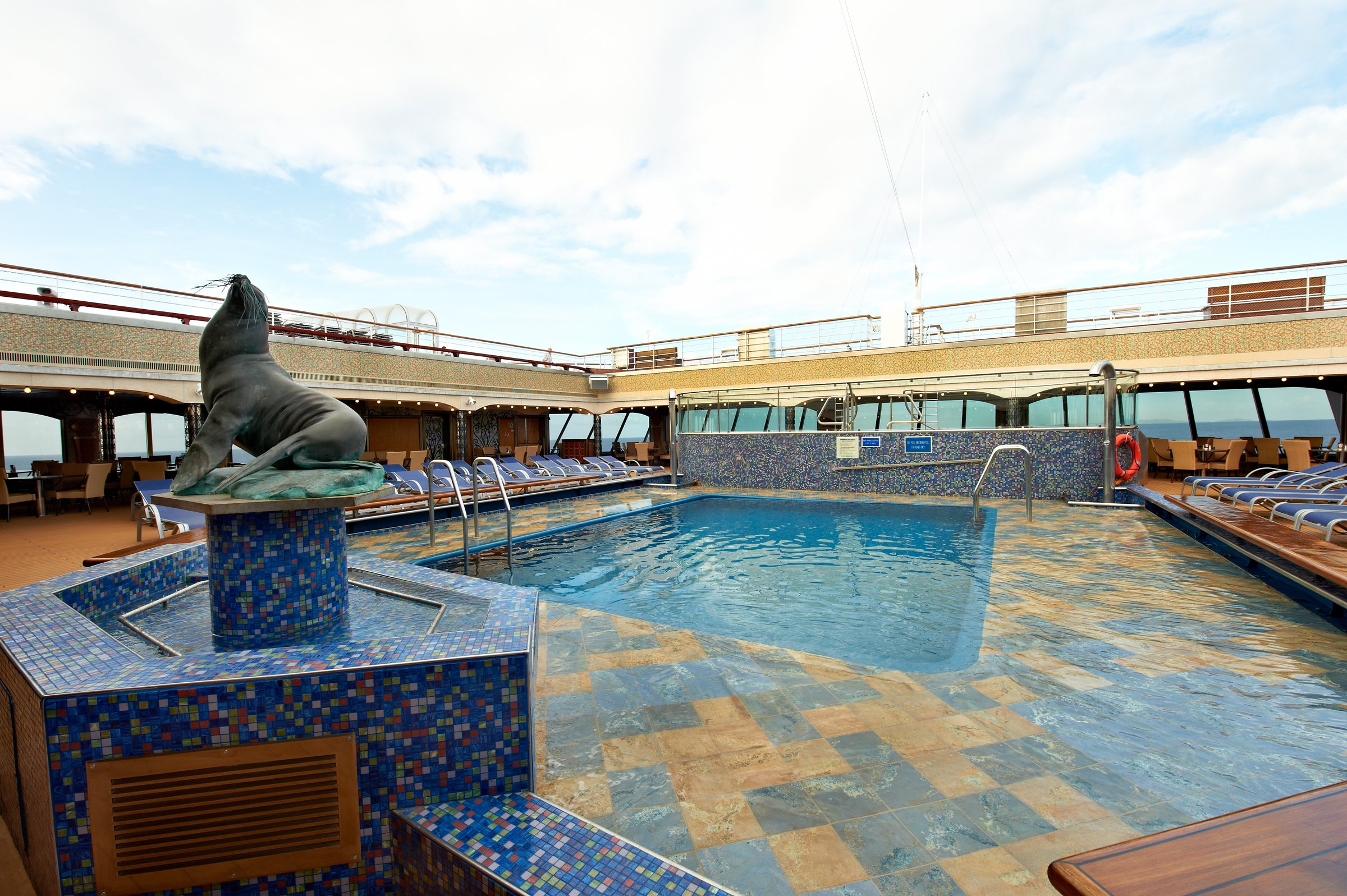 Carnival Liberty Versailles pool with a mosaic-tiled fountain statue and loungers under a bright sky