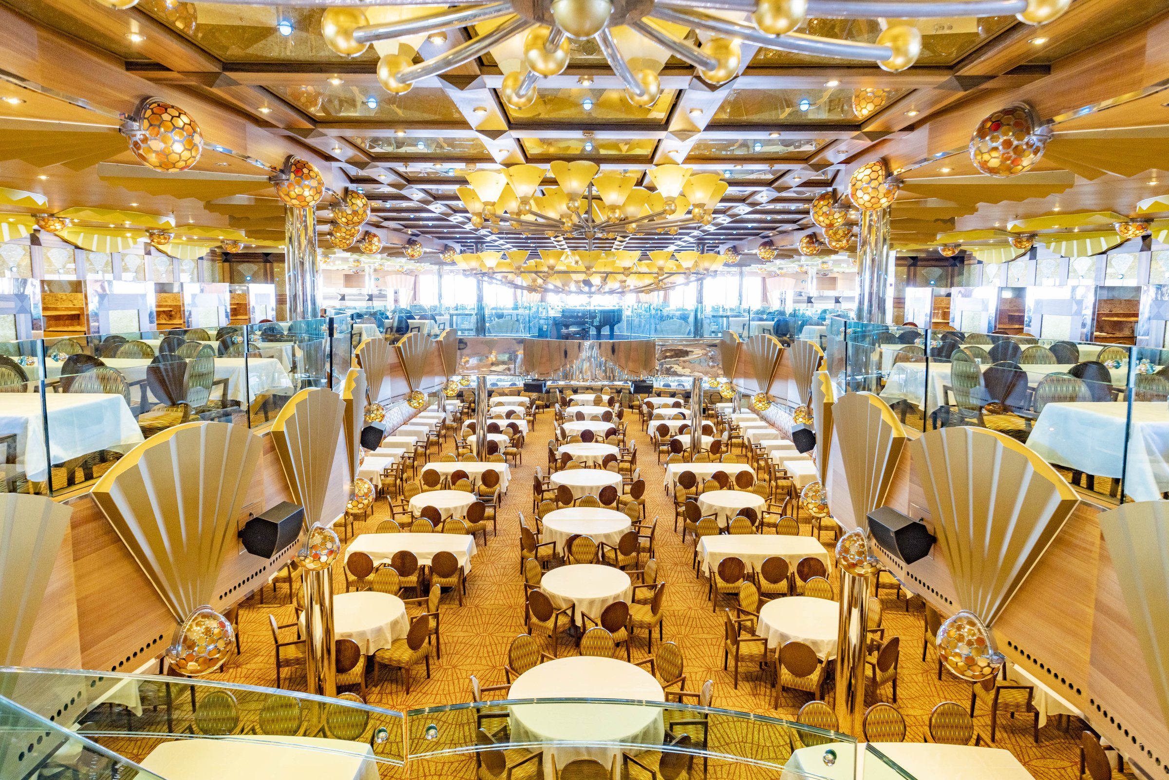 Carnival Luminosa Vela Restaurant two-level dining room with golden fan-shaped panels and chandeliers