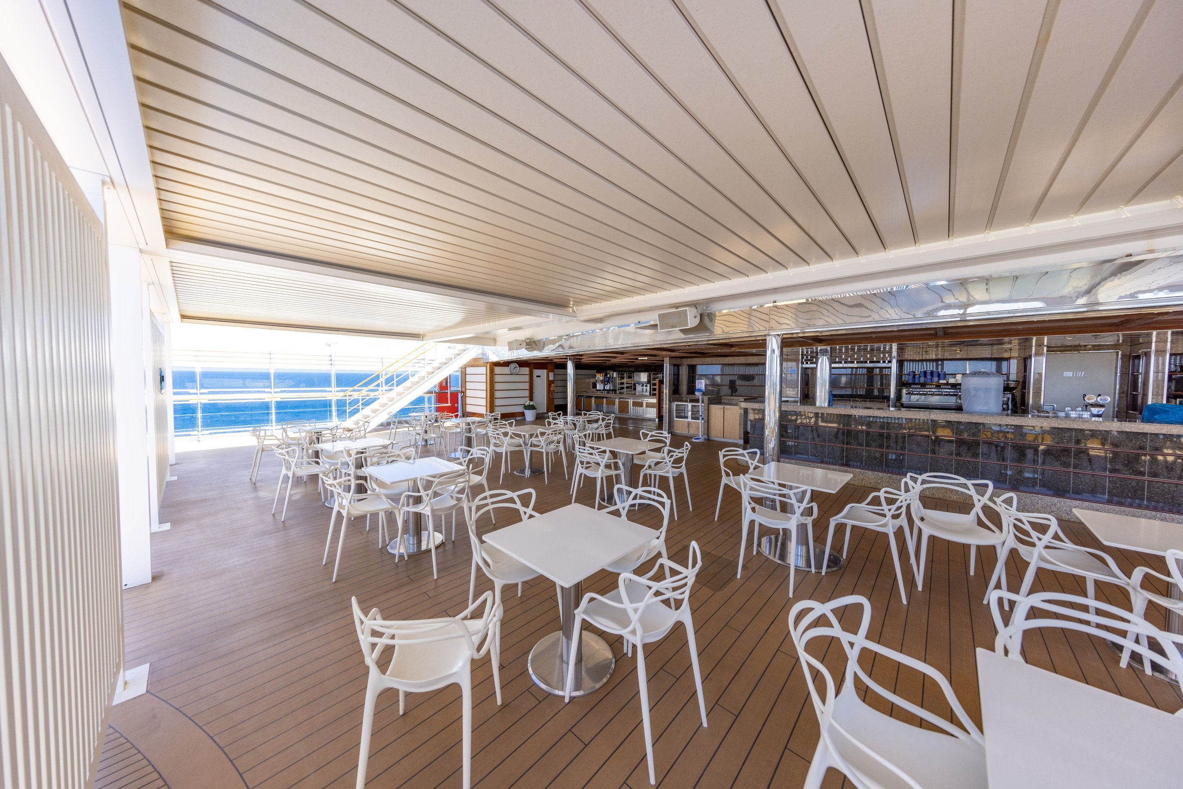 Carnival Luminosa Serenity adults-only deck with white tables and chairs and a bar at the end