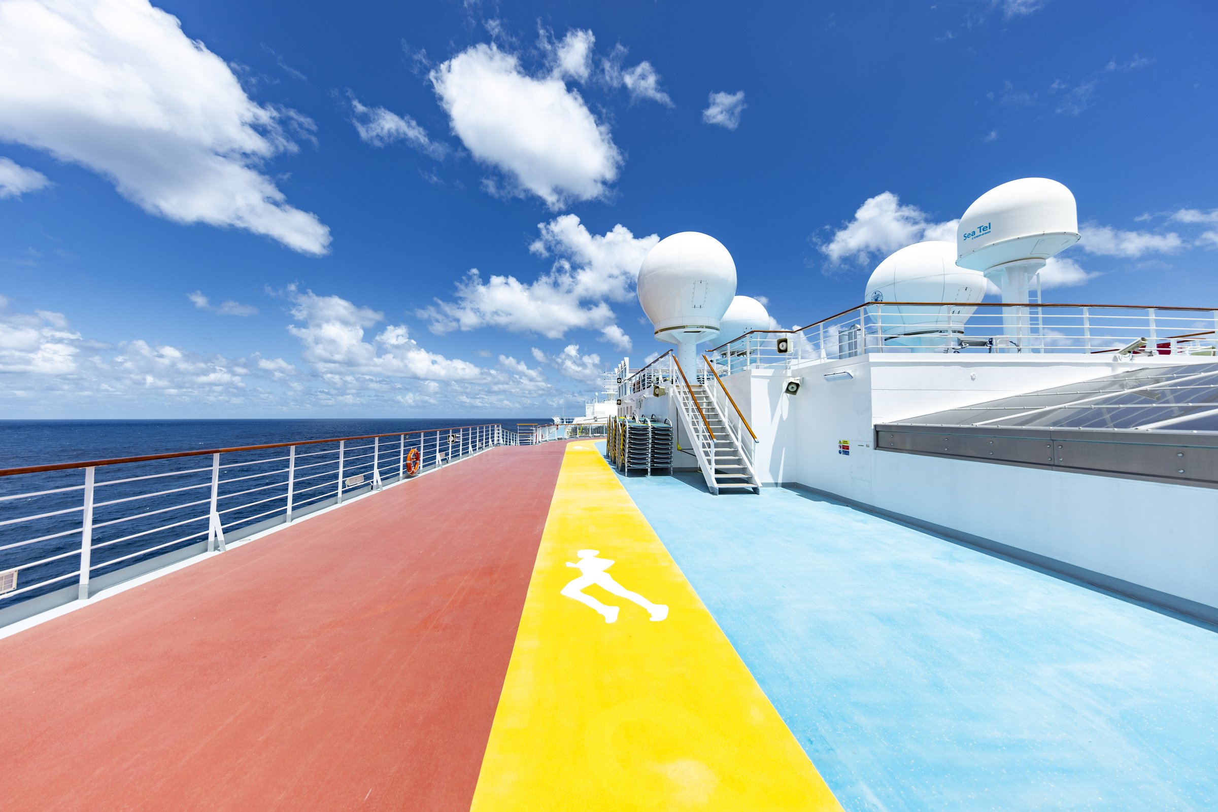 Carnival Luminosa sports deck jogging track in red, yellow and blue under a bright sky with radar domes