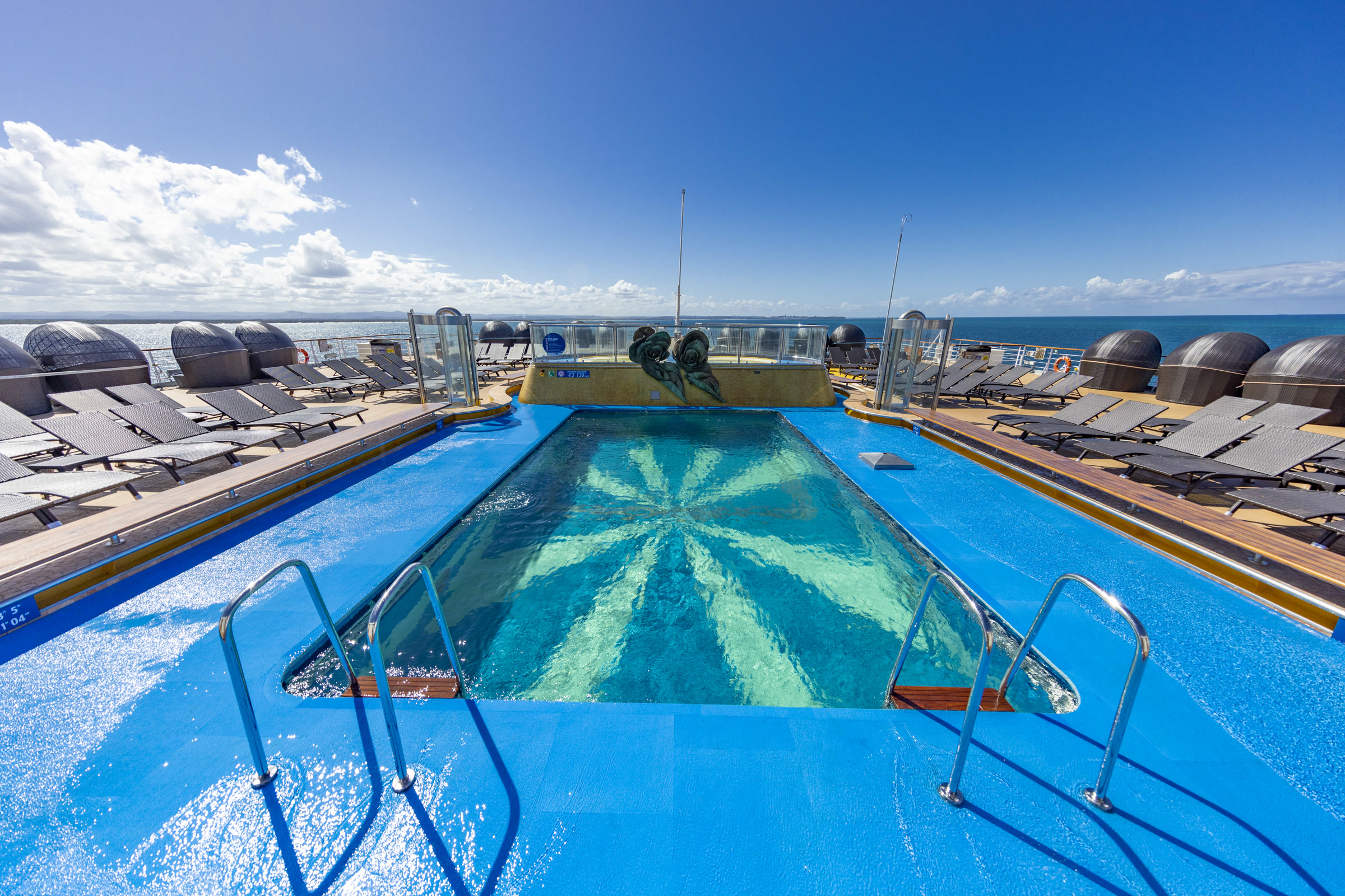 Carnival Luminosa outdoor pool deck with loungers and open ocean horizon, sunny daylight