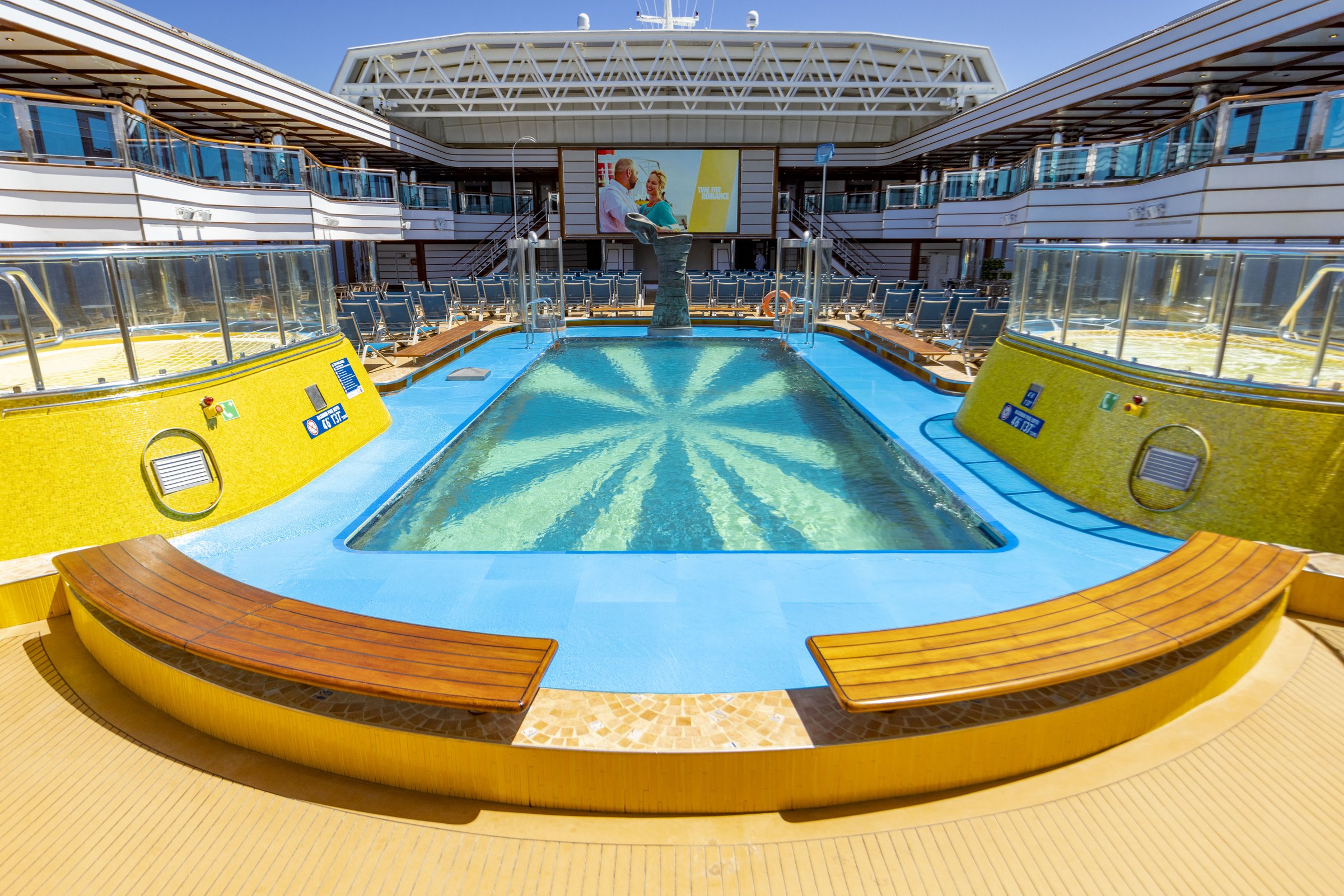 Carnival Luminosa Lido deck pool with yellow surrounds, wooden benches and the big screen behind