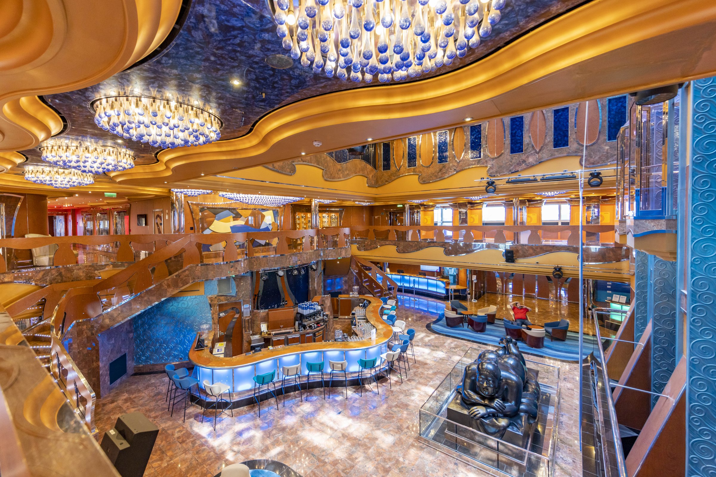 Carnival Luminosa multi-deck atrium with sweeping gold balconies, blue glass chandeliers and a central bar