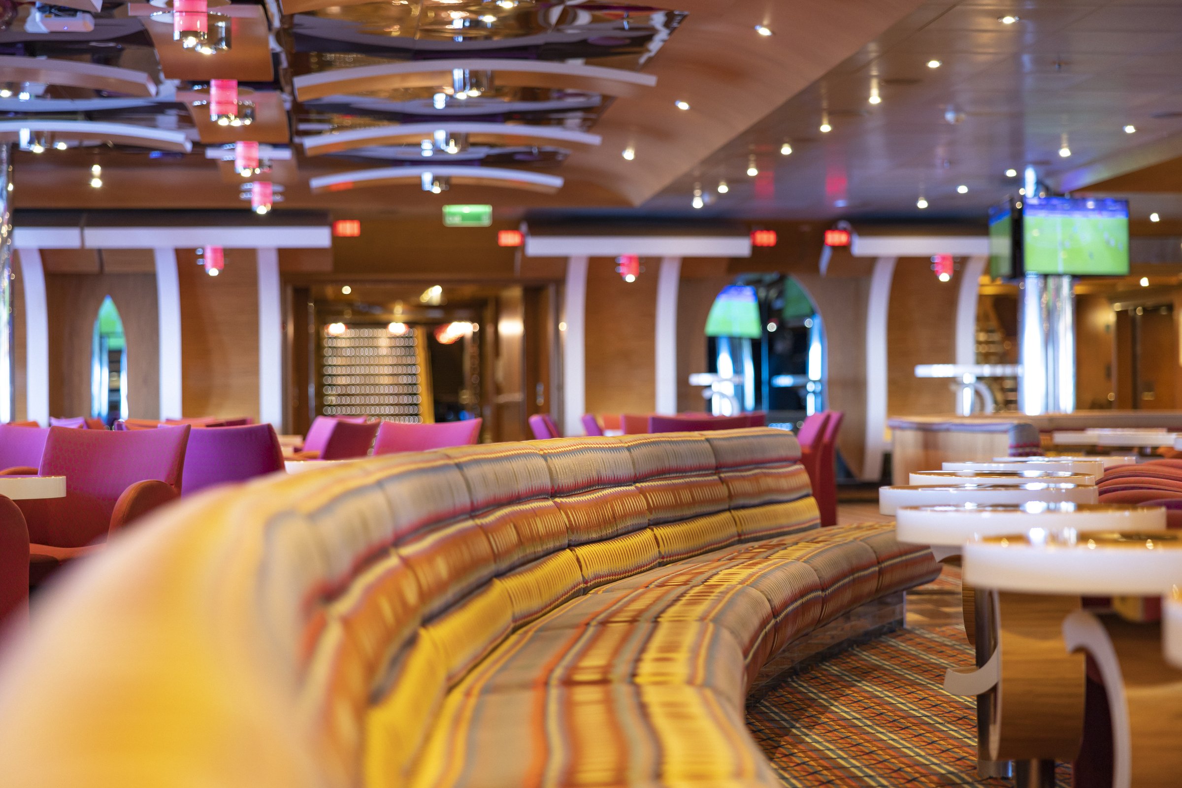 Carnival Luminosa Ocean Plaza lounge with a curved striped banquette and magenta chairs