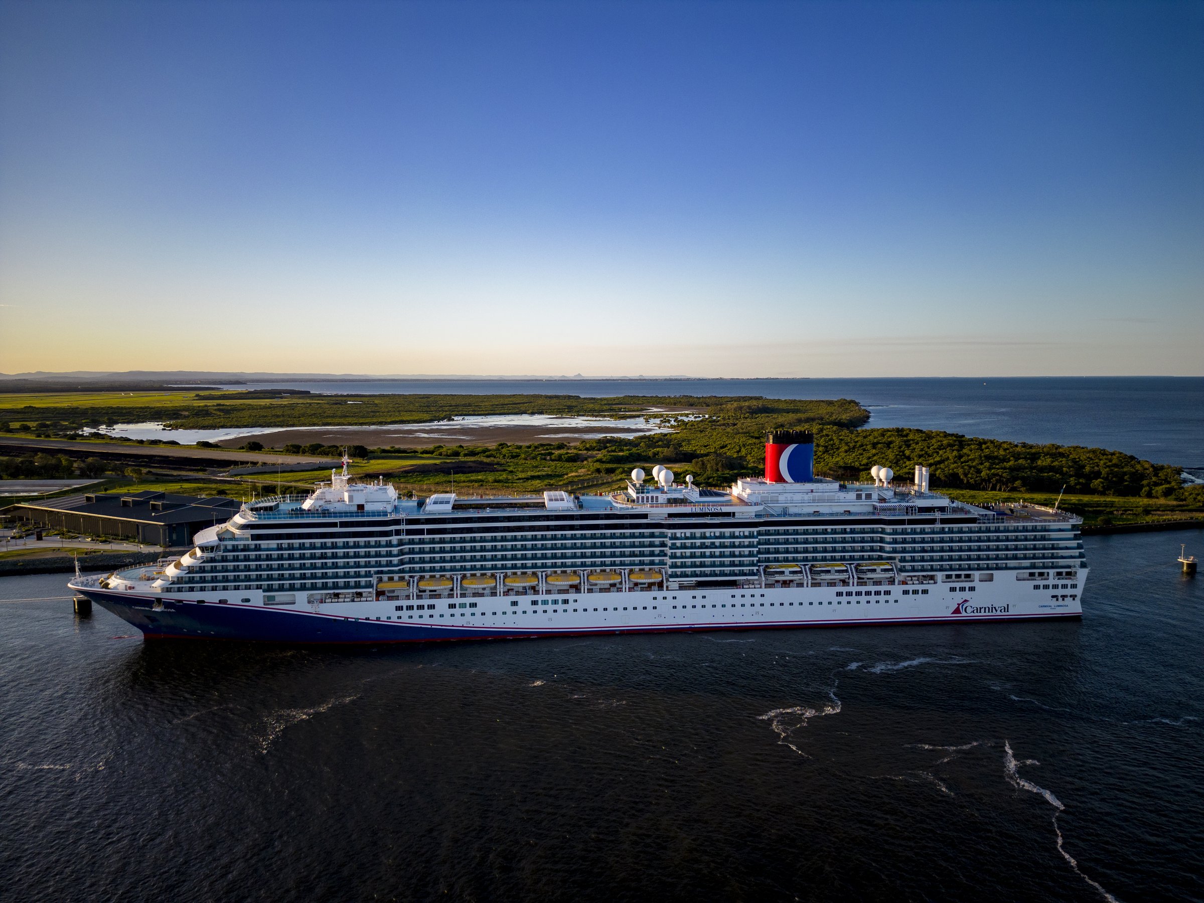 Carnival Luminosa alongside a dock at Brisbane in warm evening light, starboard side view
