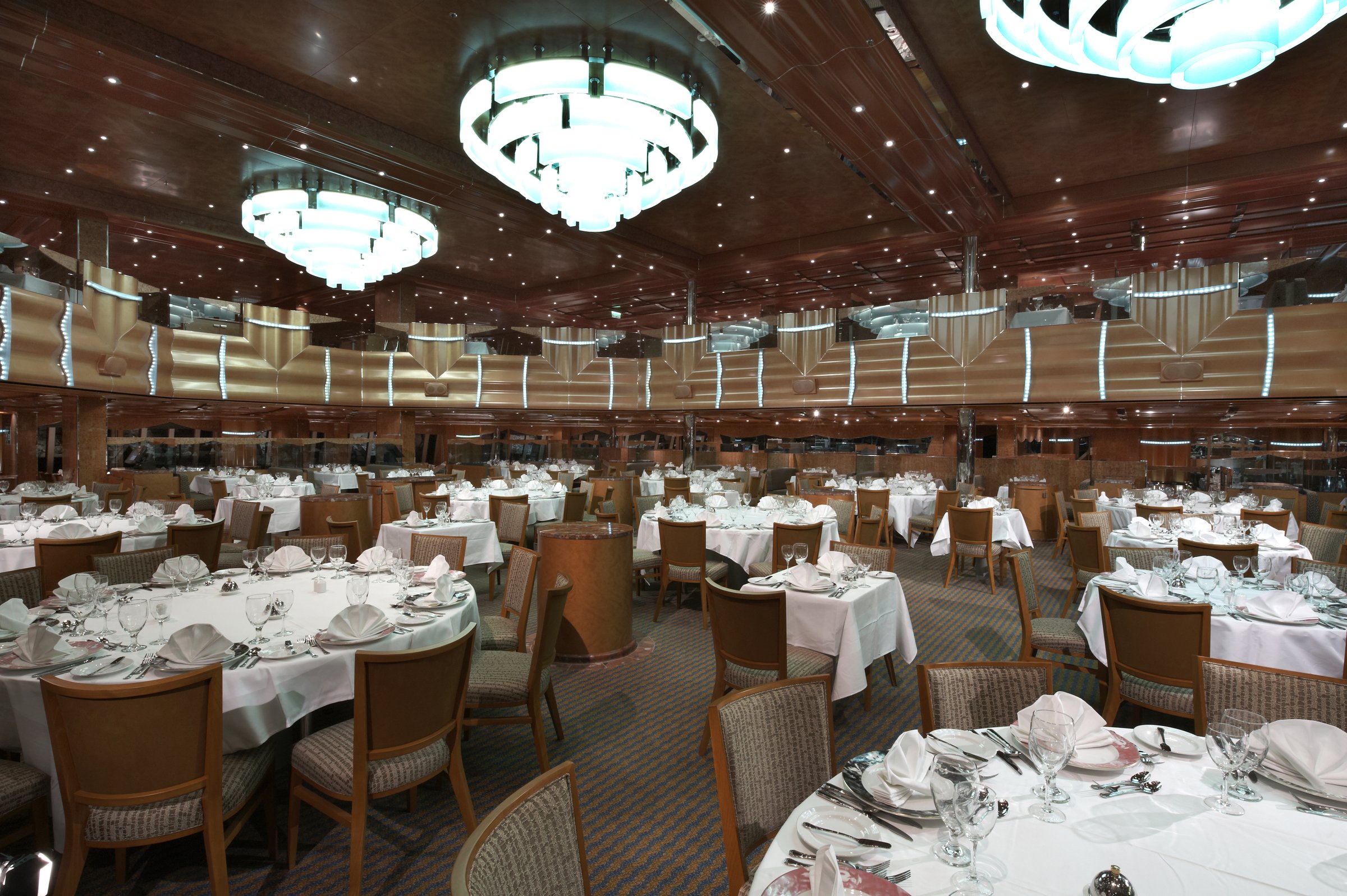 Carnival Magic Southern Lights main dining room with white-clothed tables, wicker chairs and glowing chandeliers