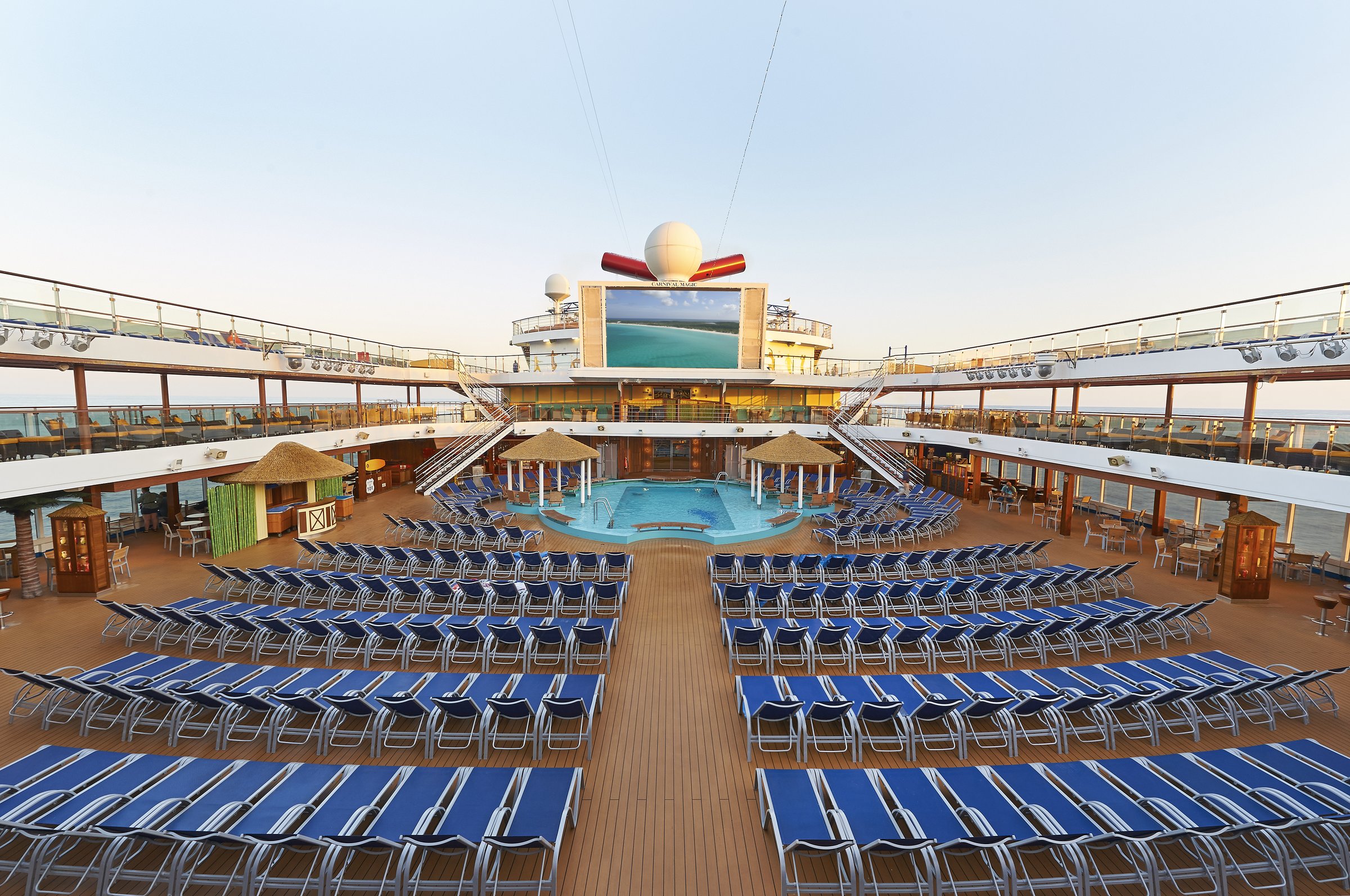 Carnival Magic midship pool deck with rows of blue loungers around the pool and the big LED screen in soft morning light