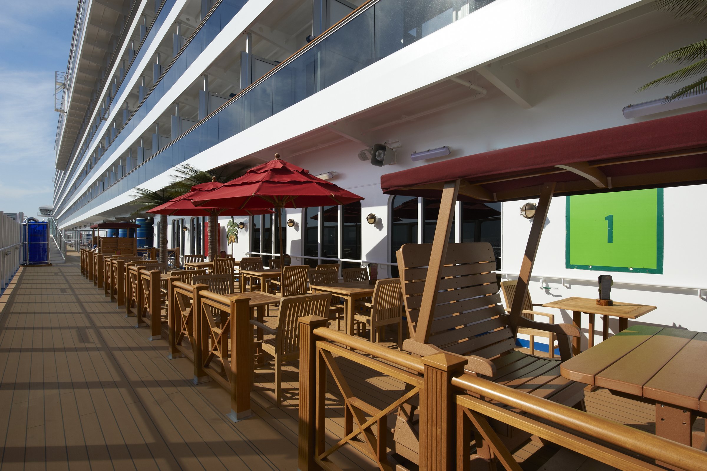Carnival Magic RedFrog Pub lanai deck with wooden tables, chairs and red umbrellas along the hull