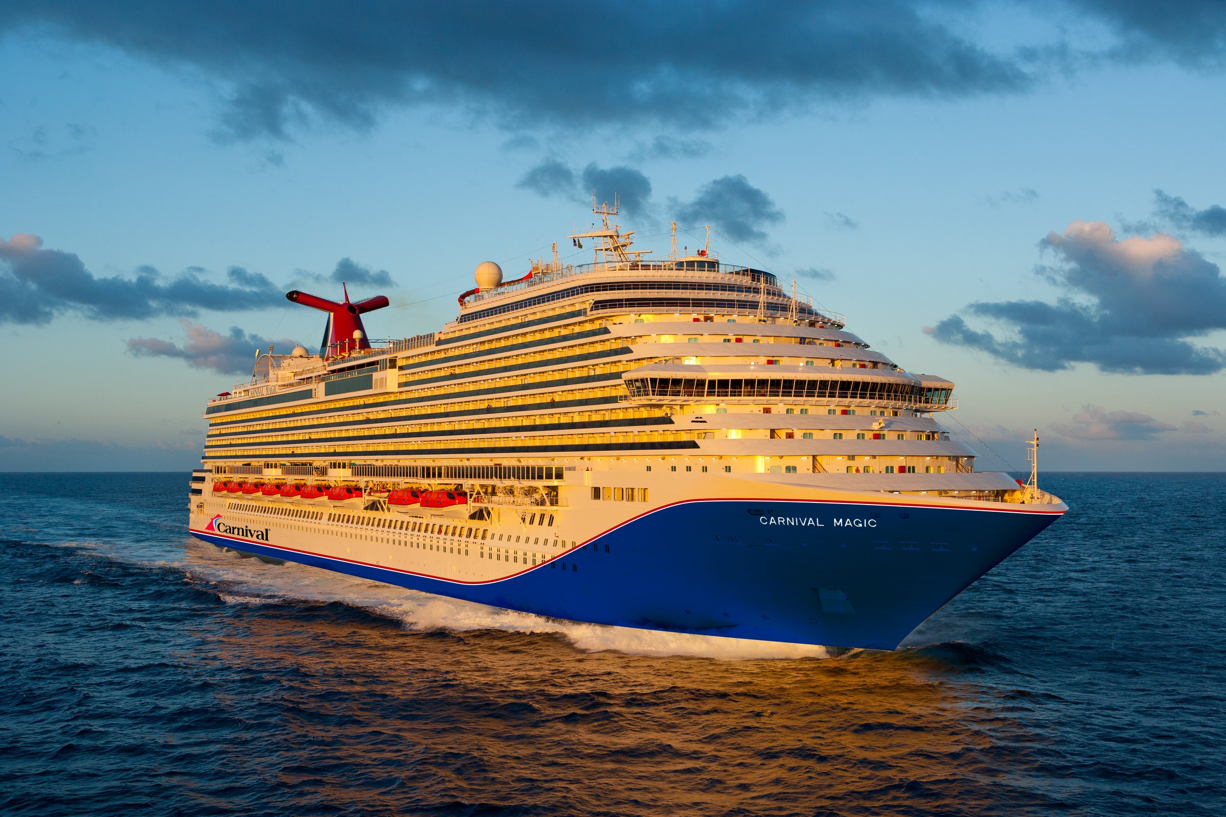 Carnival Magic cruising at sea at golden hour, bow three-quarter view with blue hull and red funnel