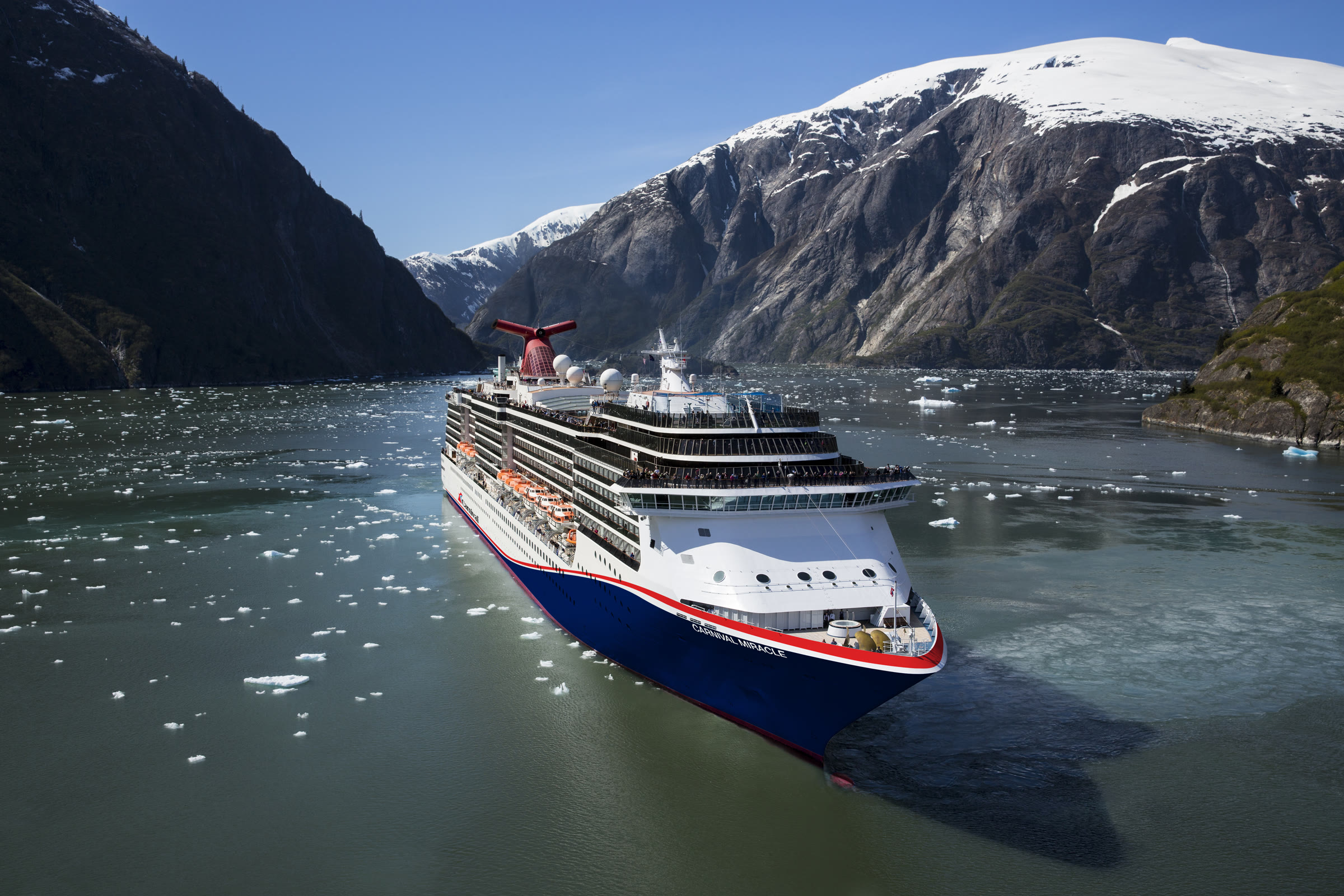 Carnival Miracle blue-hull sailing sunny Alaska waters with ice