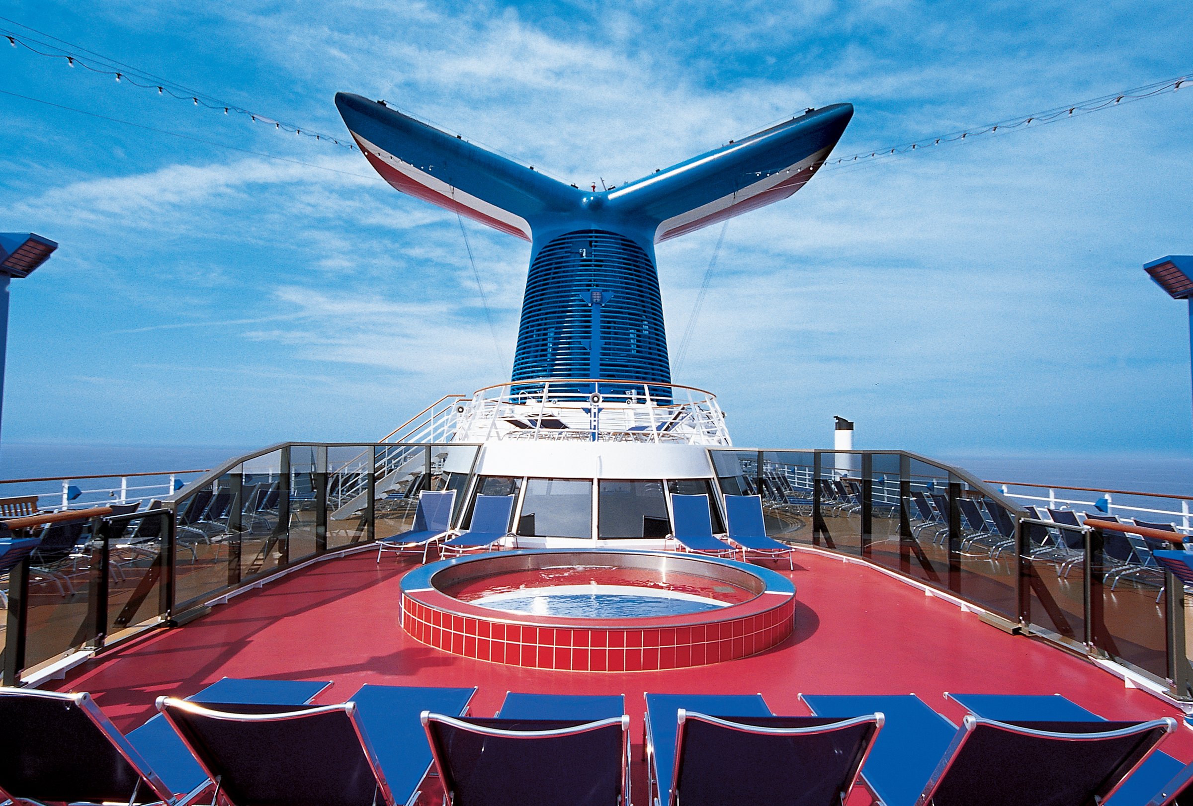 Carnival Miracle aft deck with the blue winged funnel, a red-tiled hot tub and blue loungers under a blue sky