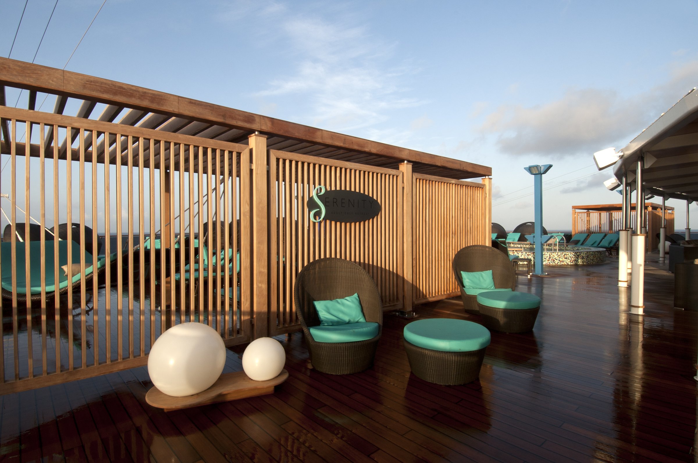 Carnival Miracle Serenity adults-only deck with wicker chairs, teal cushions and a slatted wooden screen