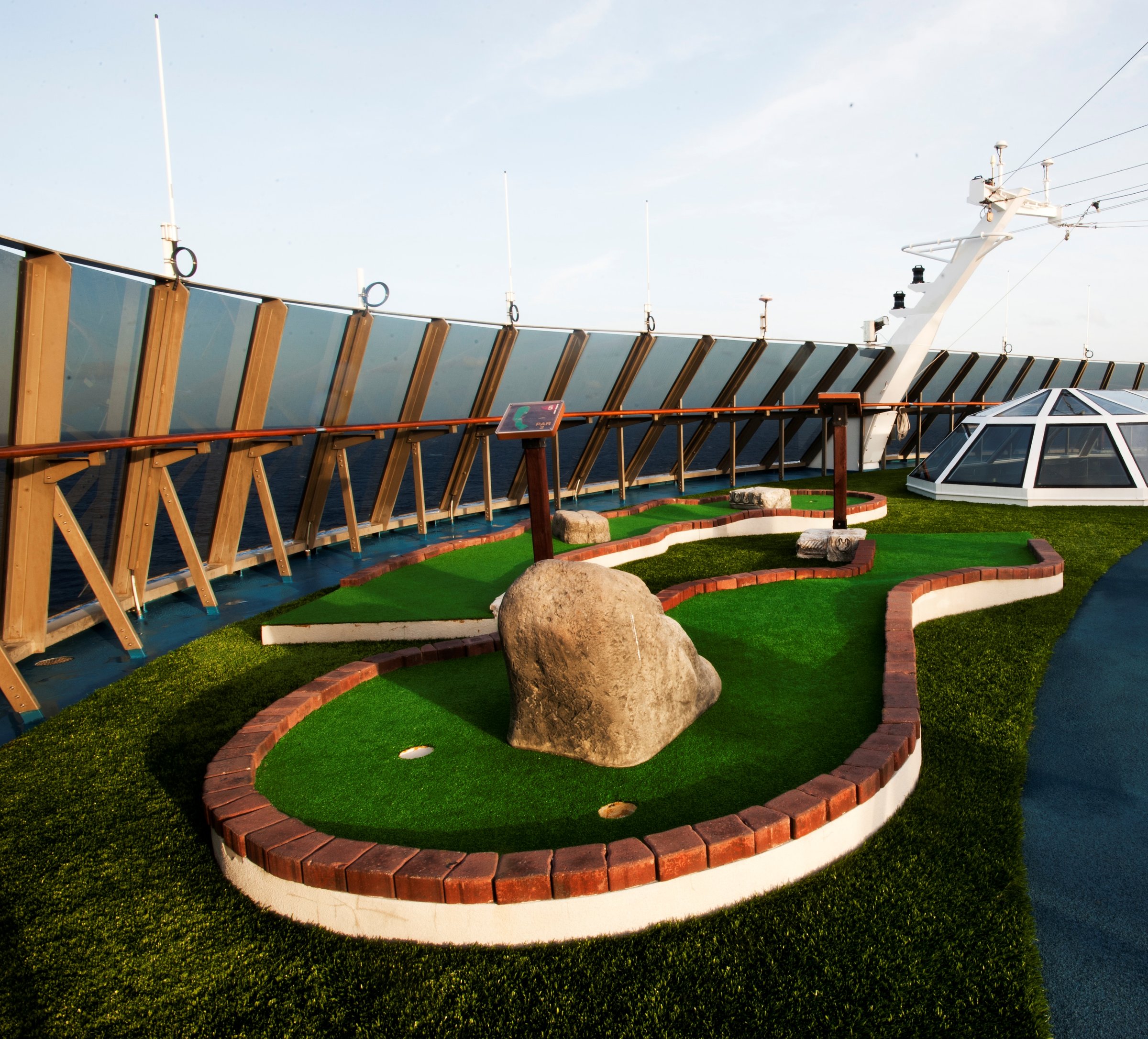 Carnival Miracle mini golf on the upper deck with artificial grass, a boulder and a deck railing