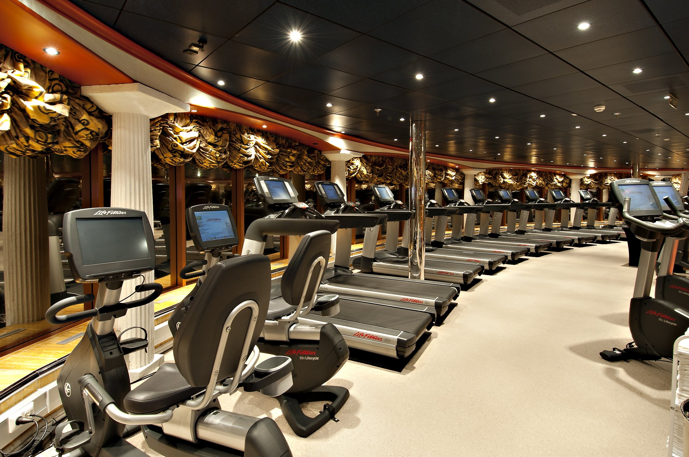 Carnival Miracle fitness centre with rows of treadmills and exercise bikes under a gilded ceiling
