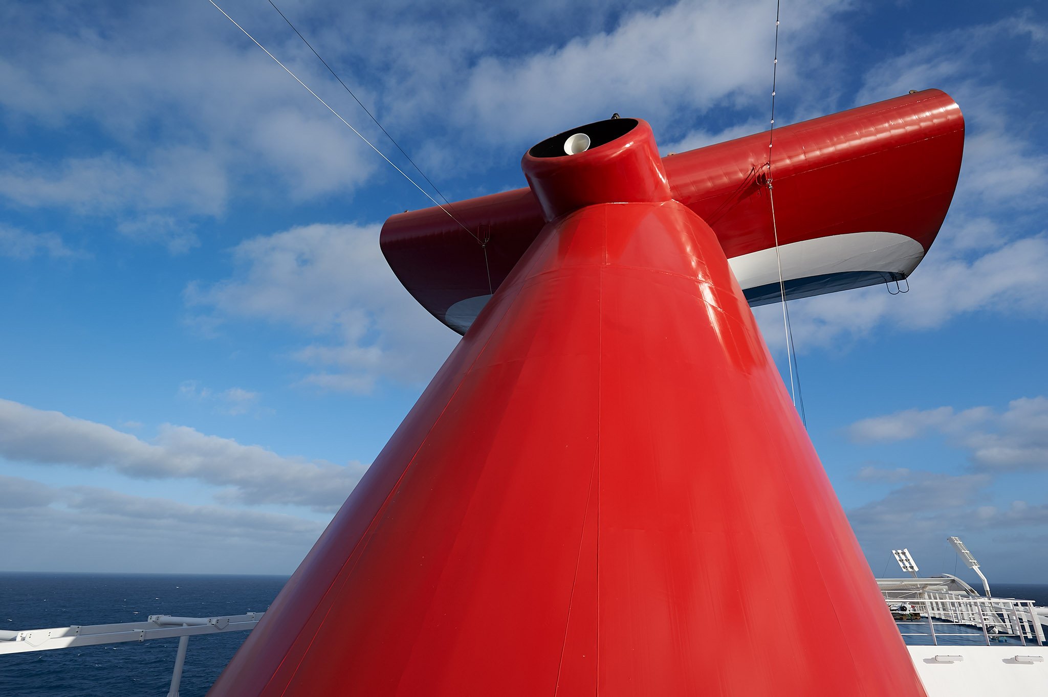 Carnival Panorama red whale-tail funnel against a blue sky with scattered clouds