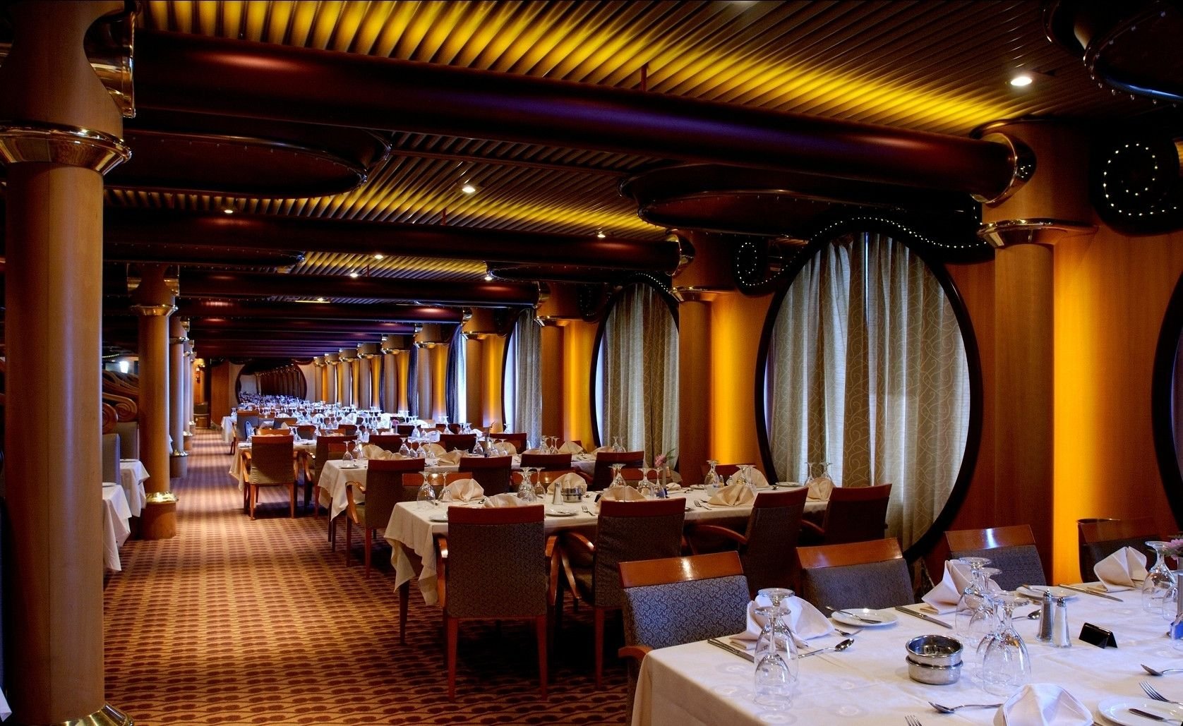Carnival Paradise Elation dining room, long room of set tables with oval curtained windows