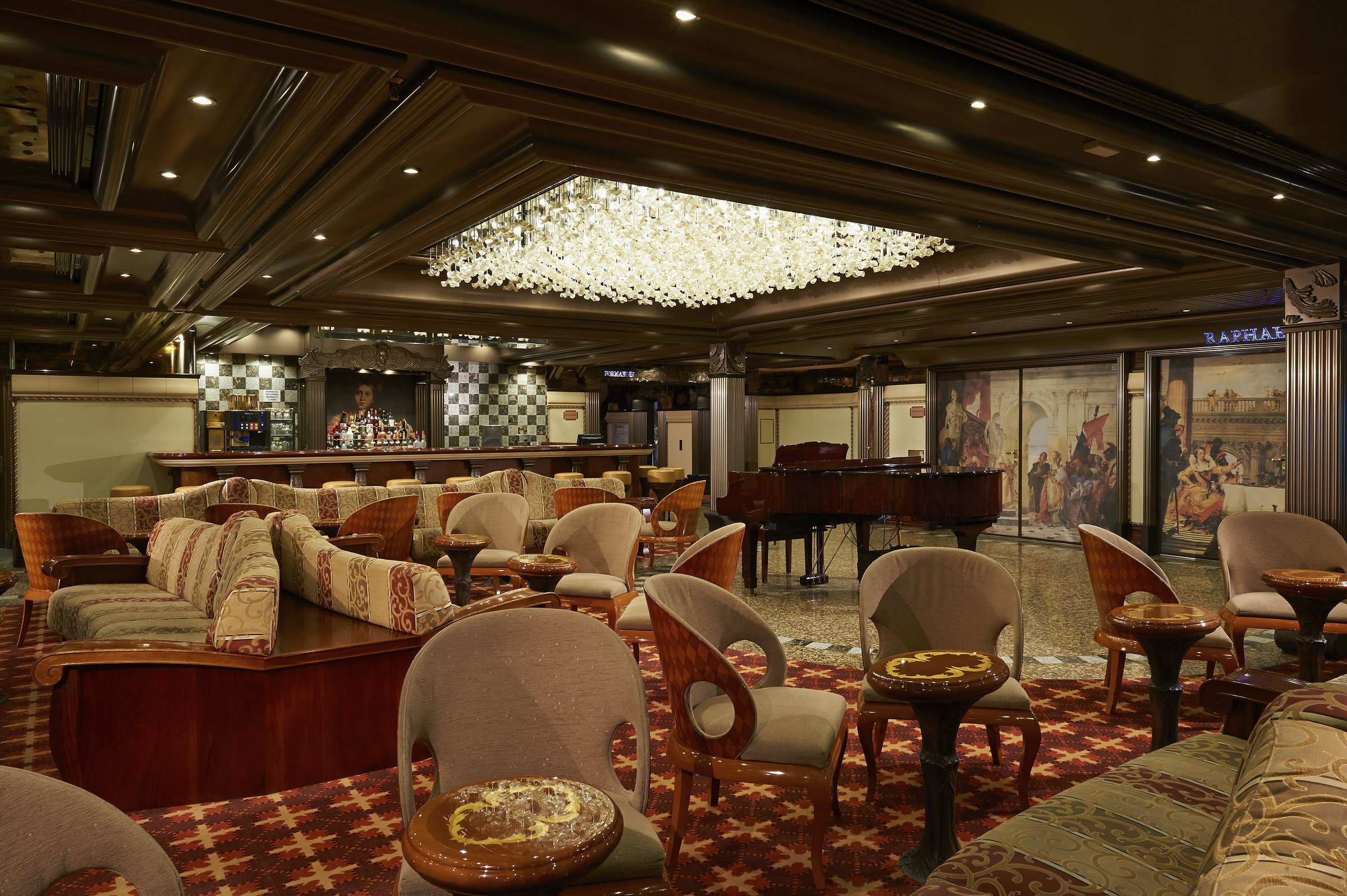 Carnival Pride Raphael lounge with patterned banquettes, armchairs, a grand piano and a crystal chandelier