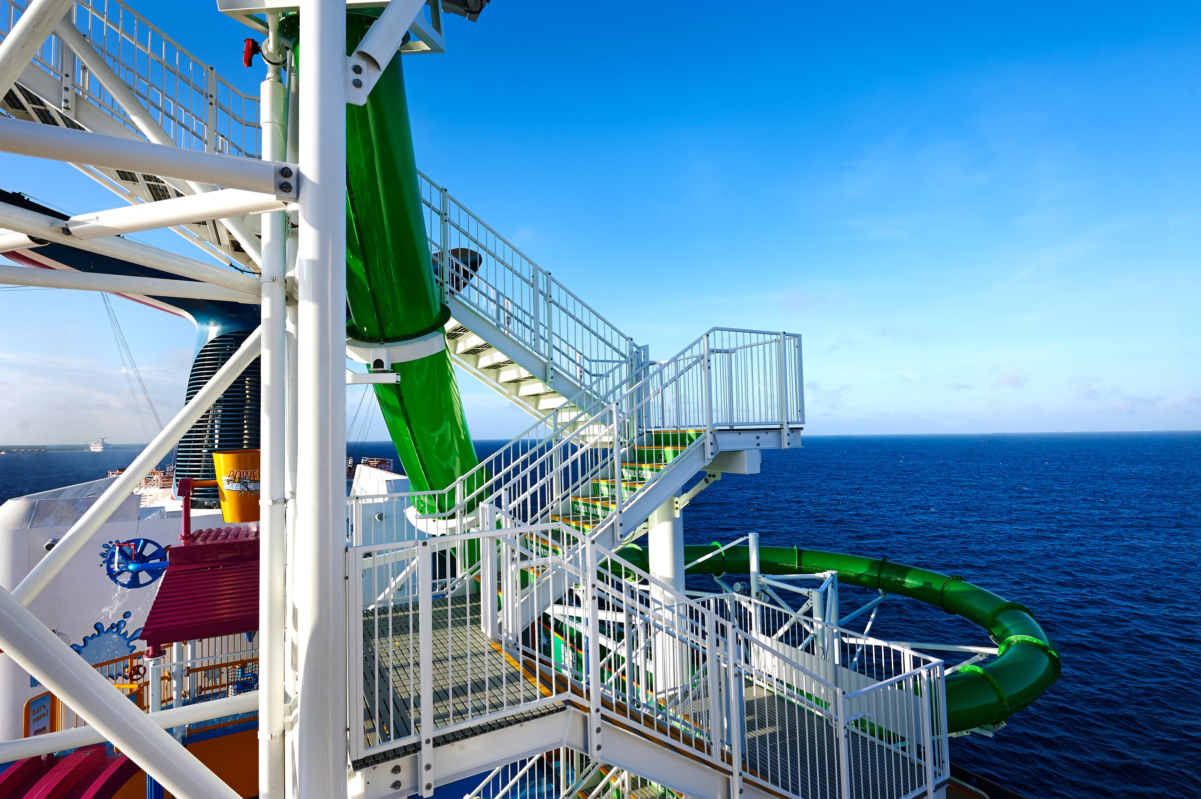 Carnival Pride WaterWorks green slide and white stair tower against a deep blue sky