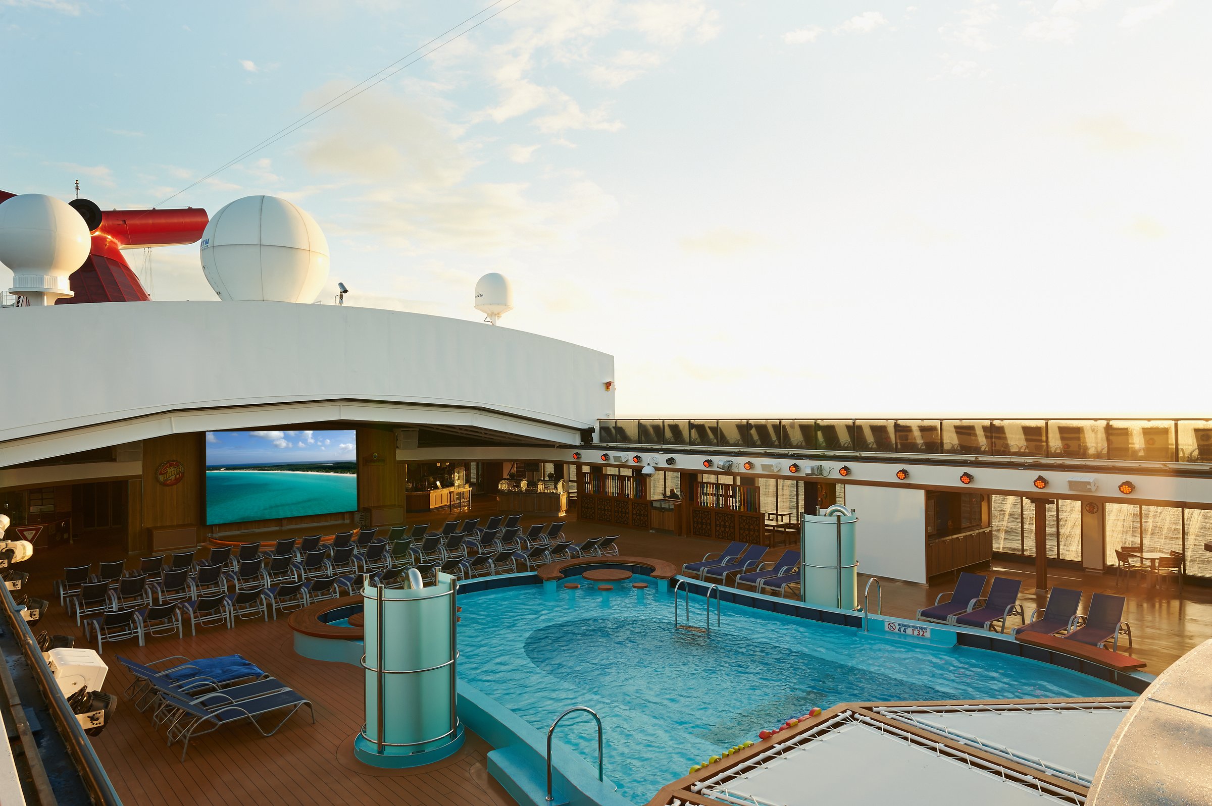 Carnival Pride Lido pool deck with loungers and a big screen in warm late-day light