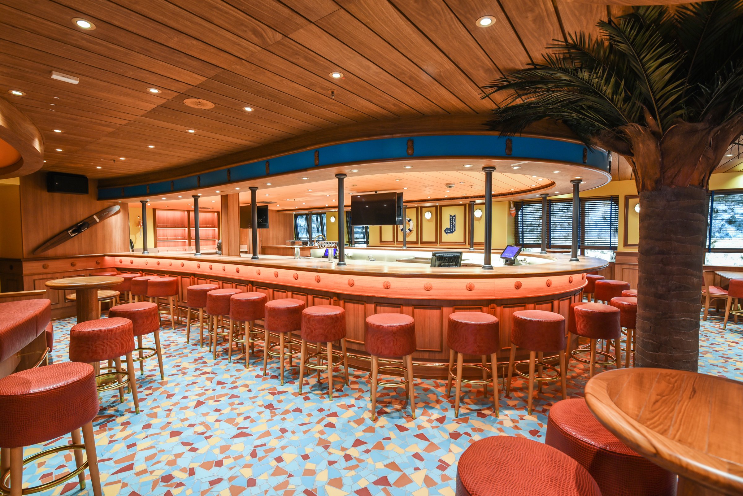 Carnival Radiance RedFrog Pub with a curved bar, red stools, a mosaic floor and a palm tree