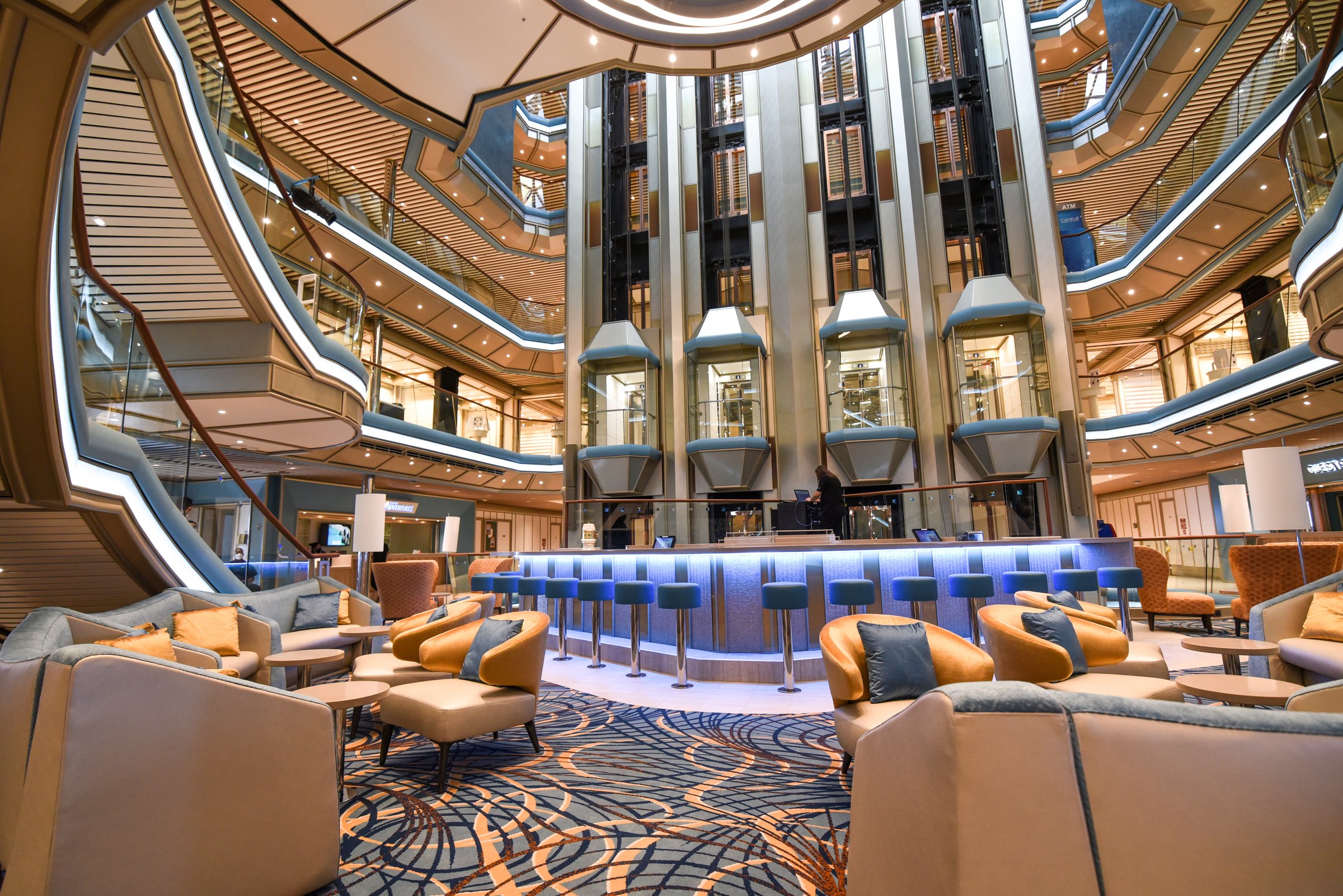Carnival Radiance multi-deck atrium with glass elevators, a blue-lit central bar and lounge armchairs