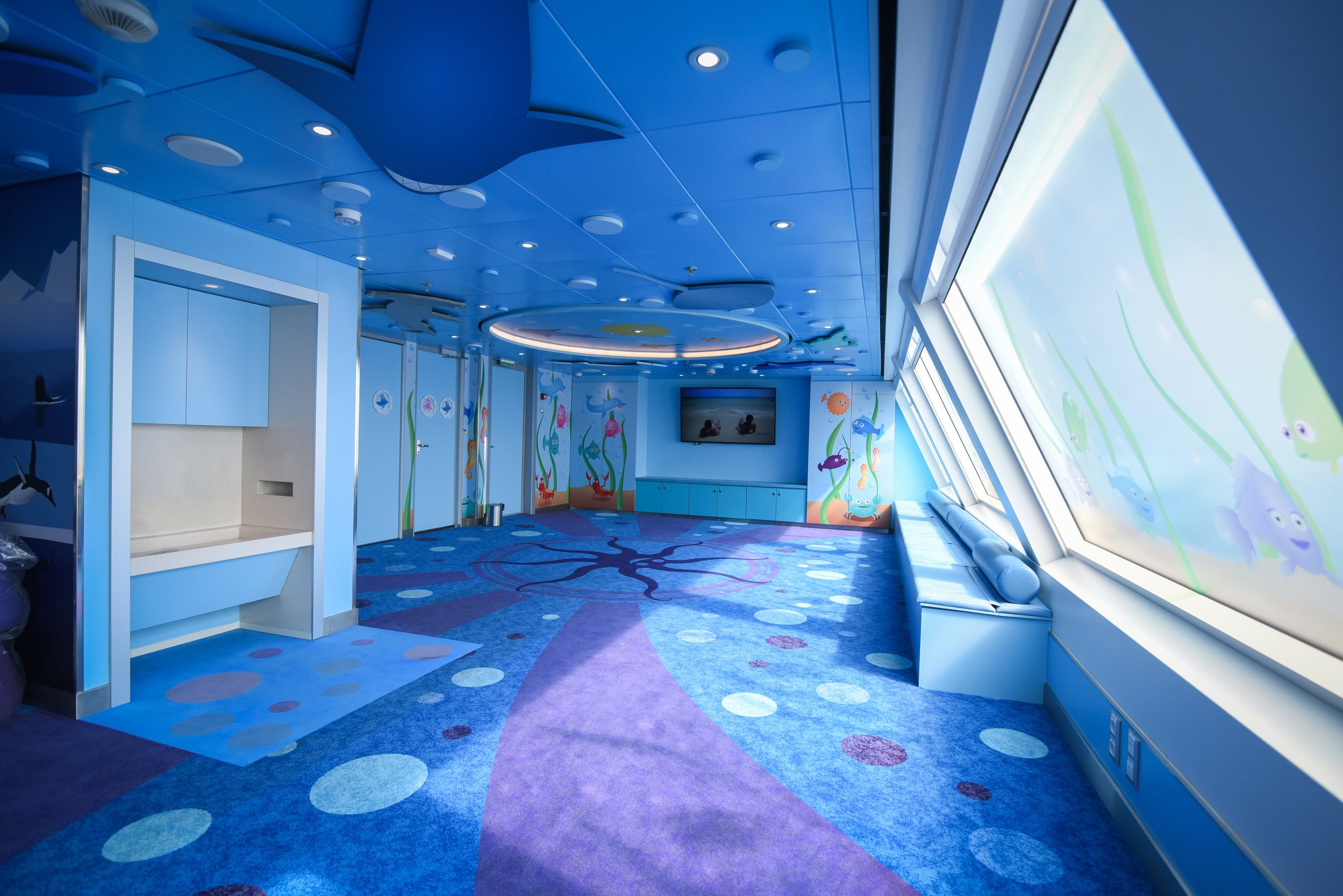 Carnival Radiance Camp Ocean kids club with an ocean-themed carpet, window seat and sea-creature murals