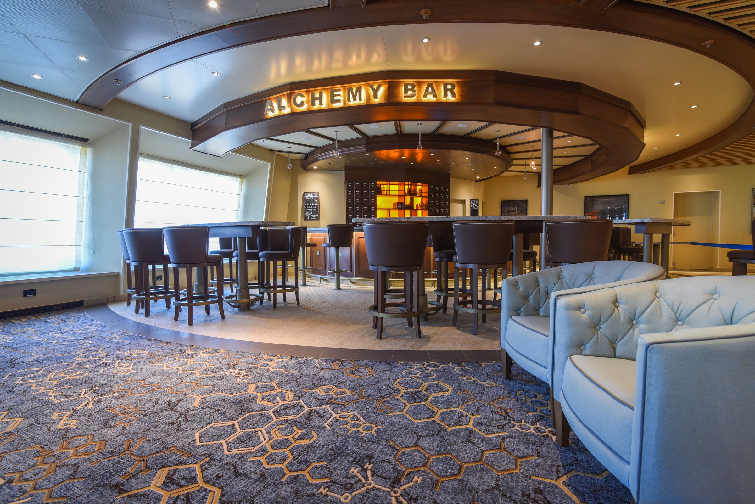 Carnival Radiance Alchemy Bar with tall chairs, a circular back bar and pale tufted armchairs