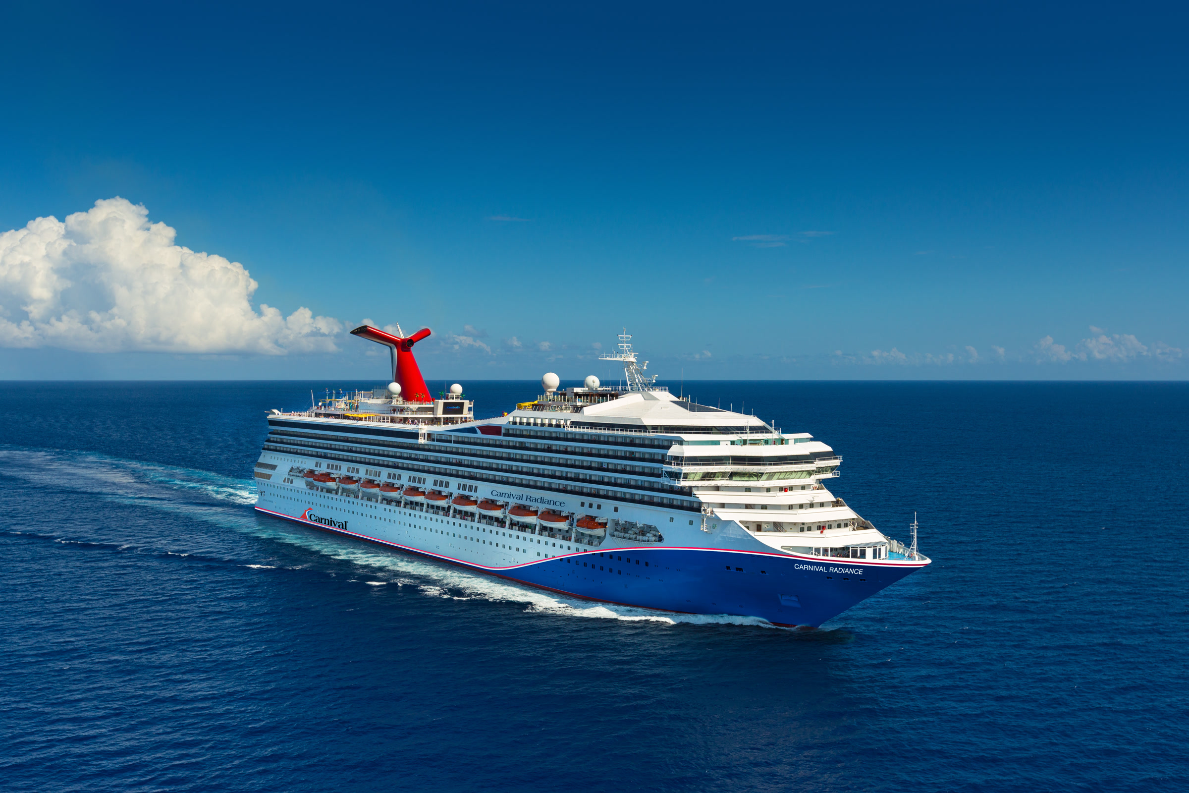 Carnival Radiance blue-hull aerial exterior in sunny open water, bright daylight