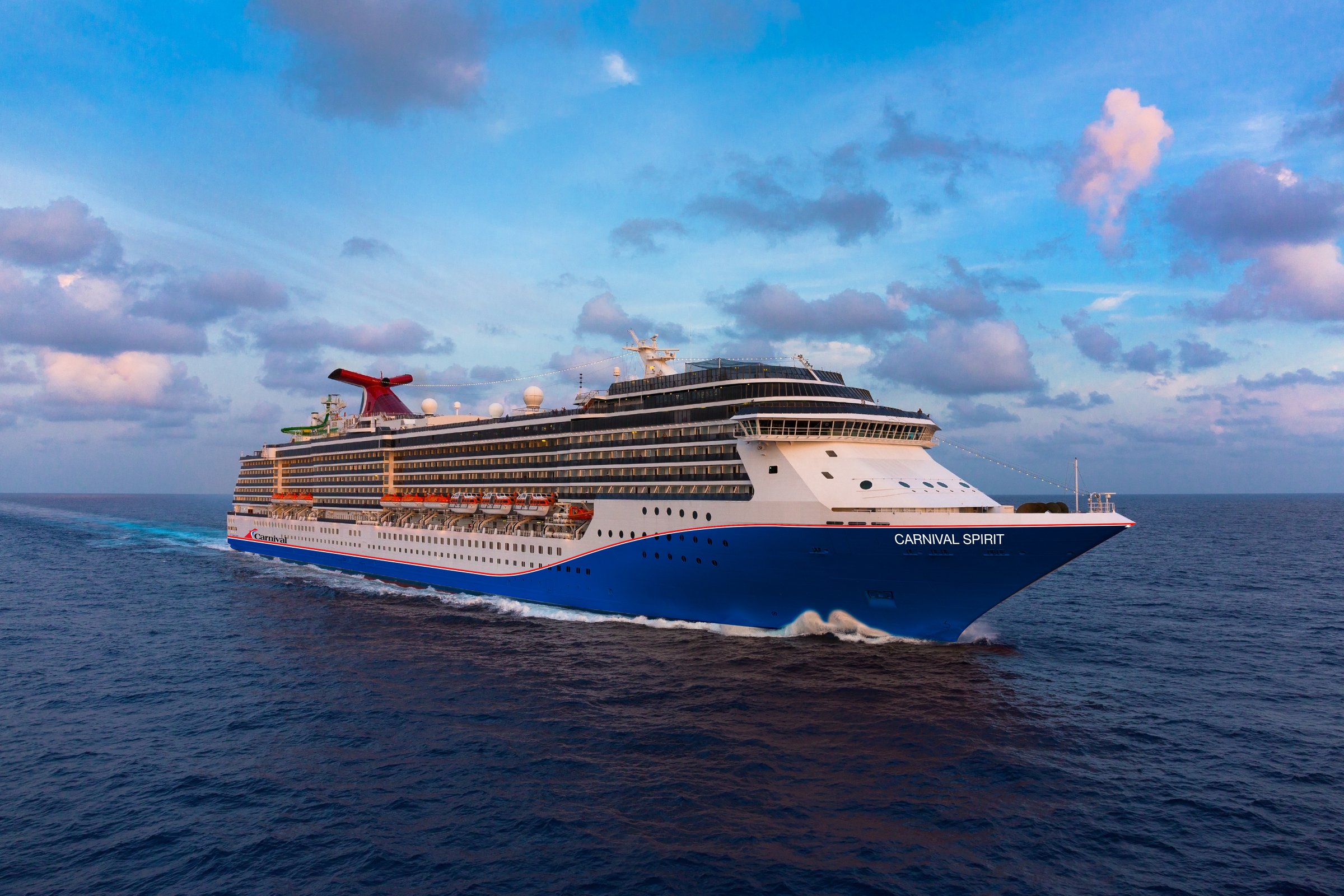 Carnival Spirit blue-hulled ship underway at sea beneath a bright sky with scattered clouds