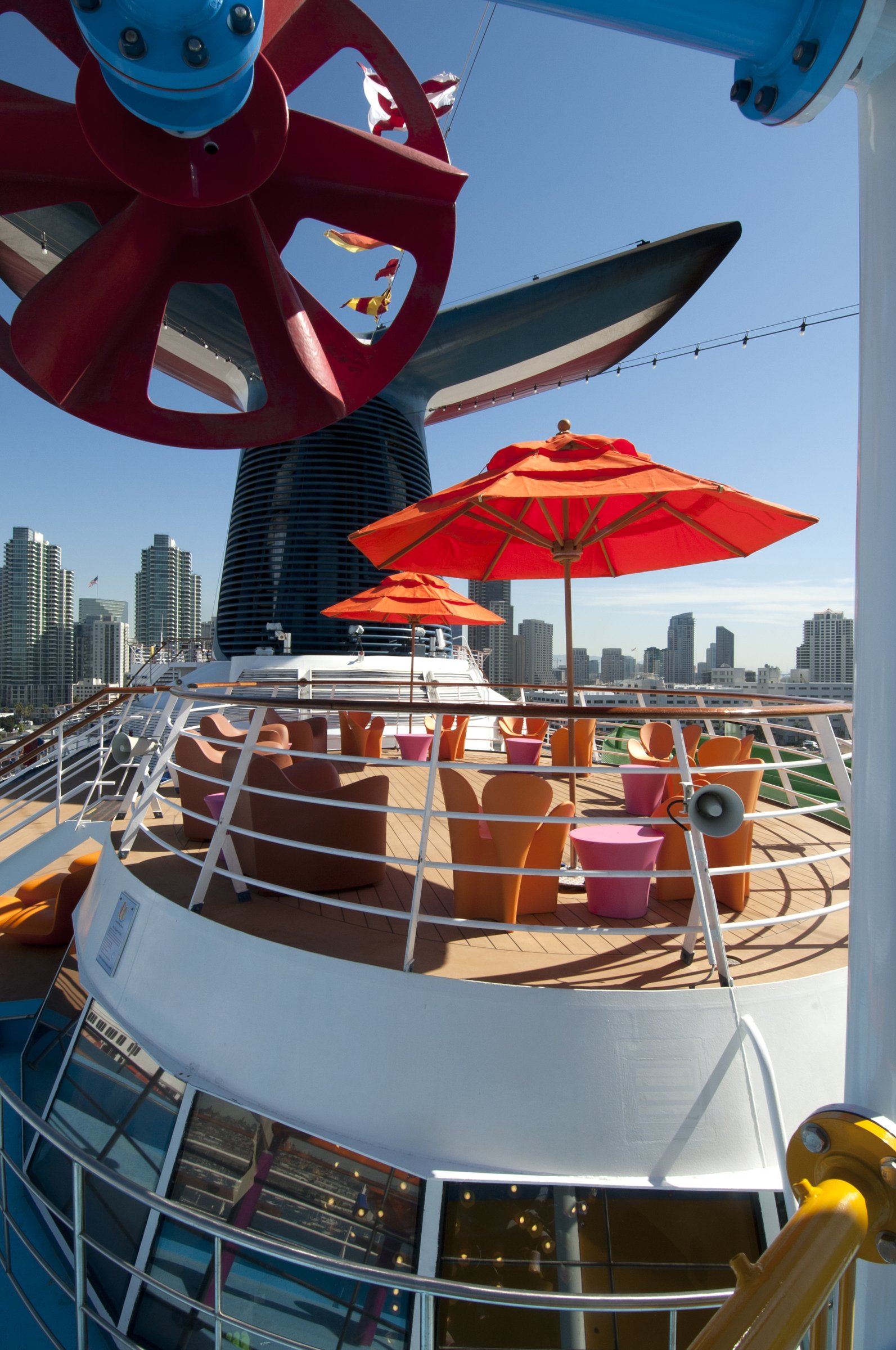Carnival Spirit funnel-base deck with orange umbrellas and seating, with a city skyline behind