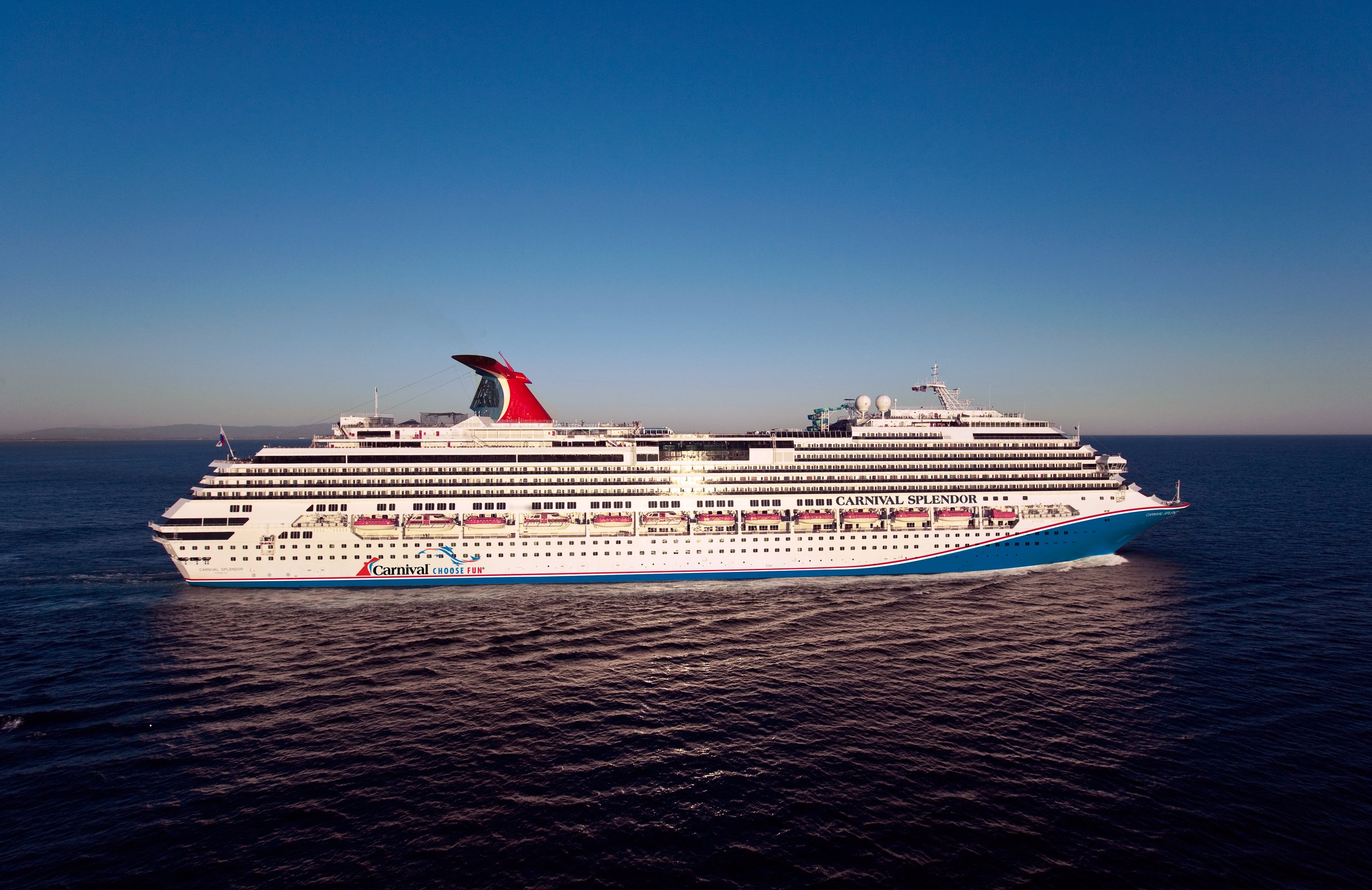 Carnival Splendor broadside at sea in warm low sunlight, with its red funnel and calm deep-blue water