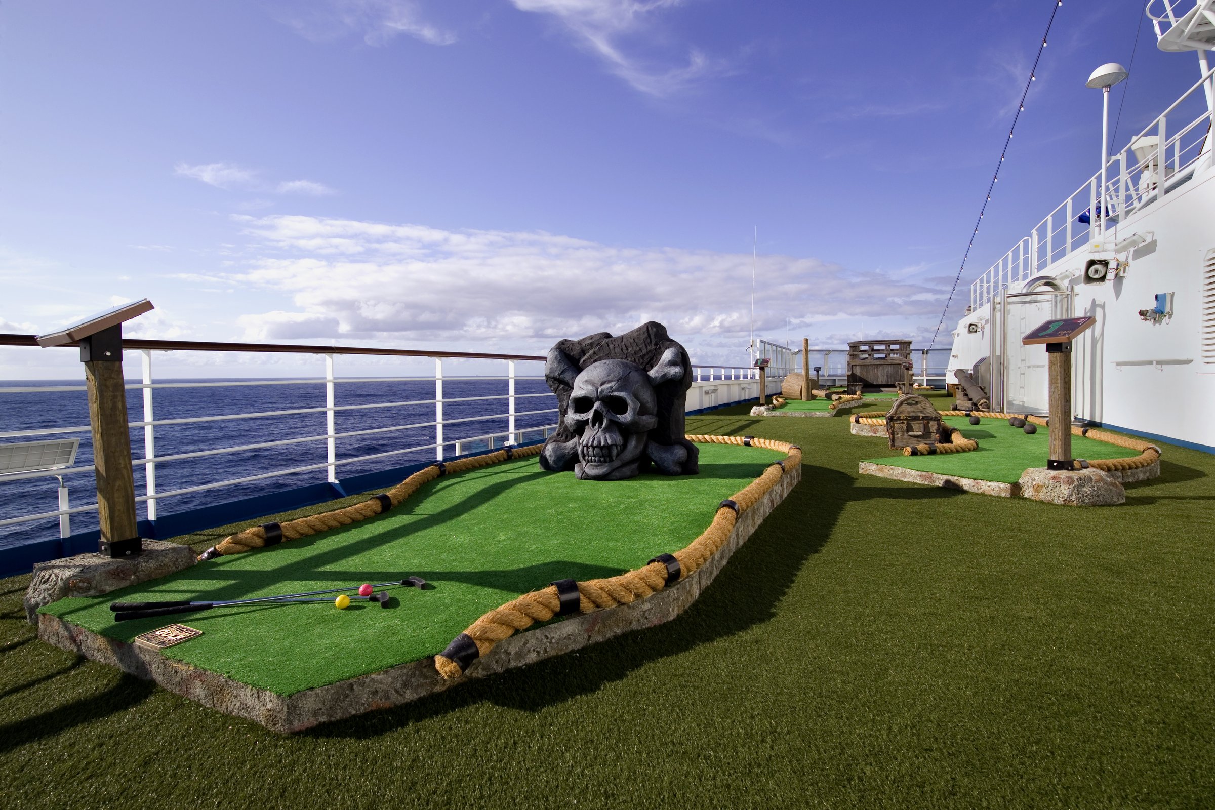 Carnival Splendor pirate-themed mini golf with a skull boulder on the upper deck under a blue sky